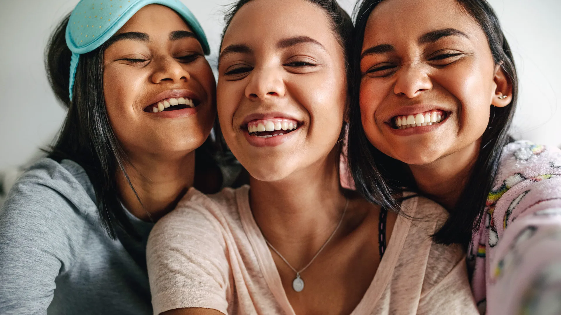 A photo of three teenage girls laughing with their heads pressed together at a sleepover