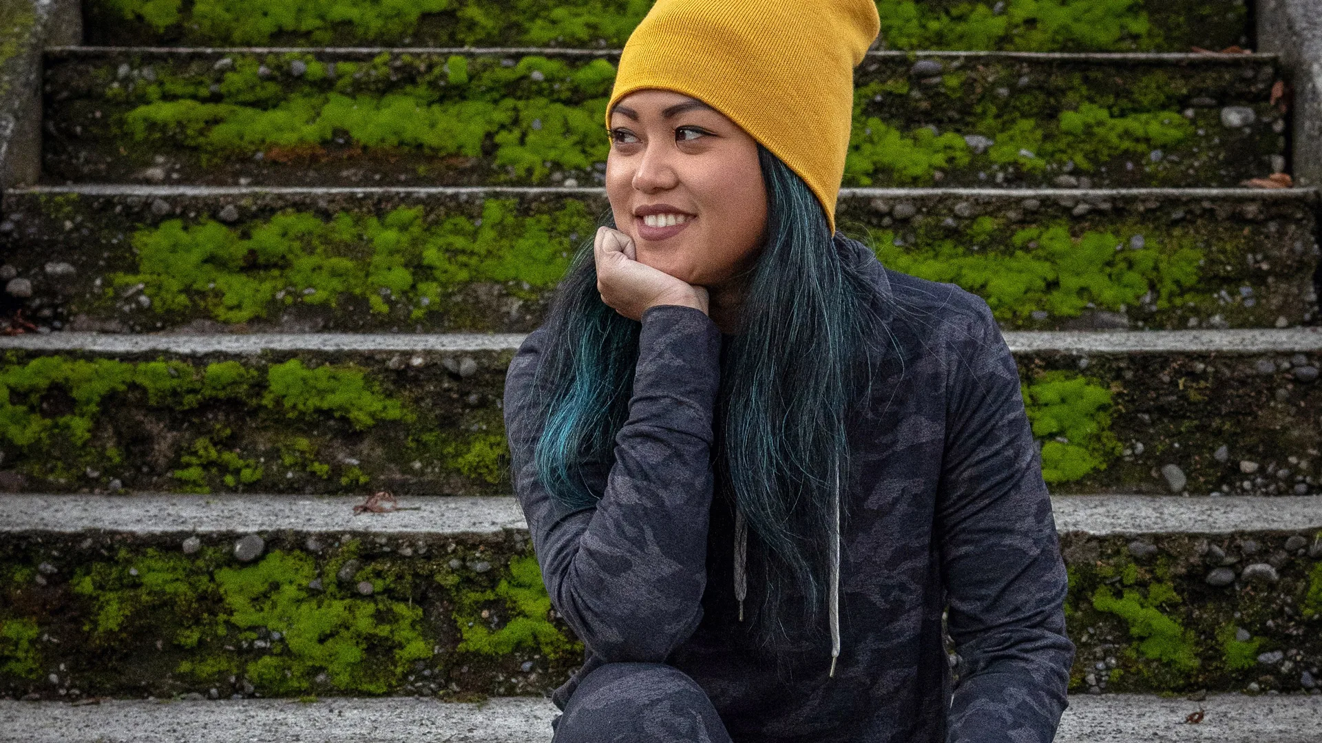 Girl with long hair and yellow beanie sitting on mossy steps