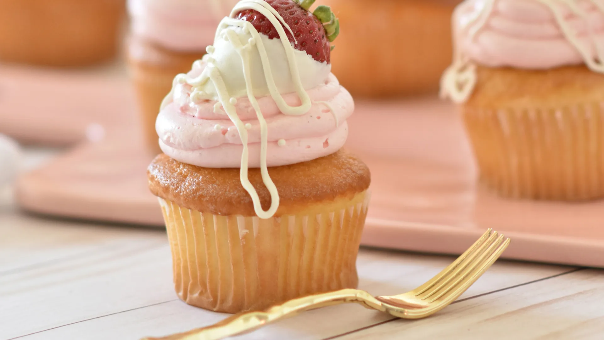 Iced cupcake with pink icing and cream on top with strawberry