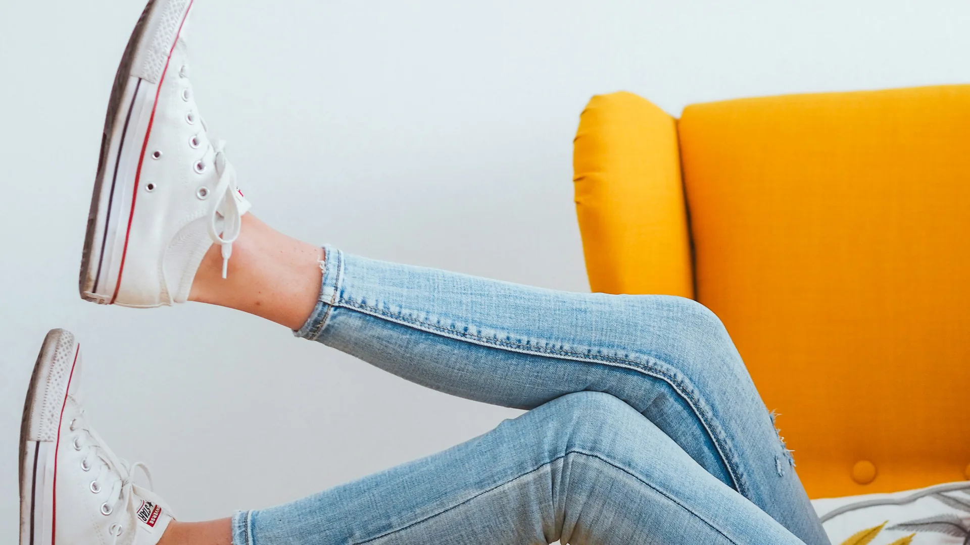 Photo of two legs over a yellow sofa arm wearing blue jeans and converse