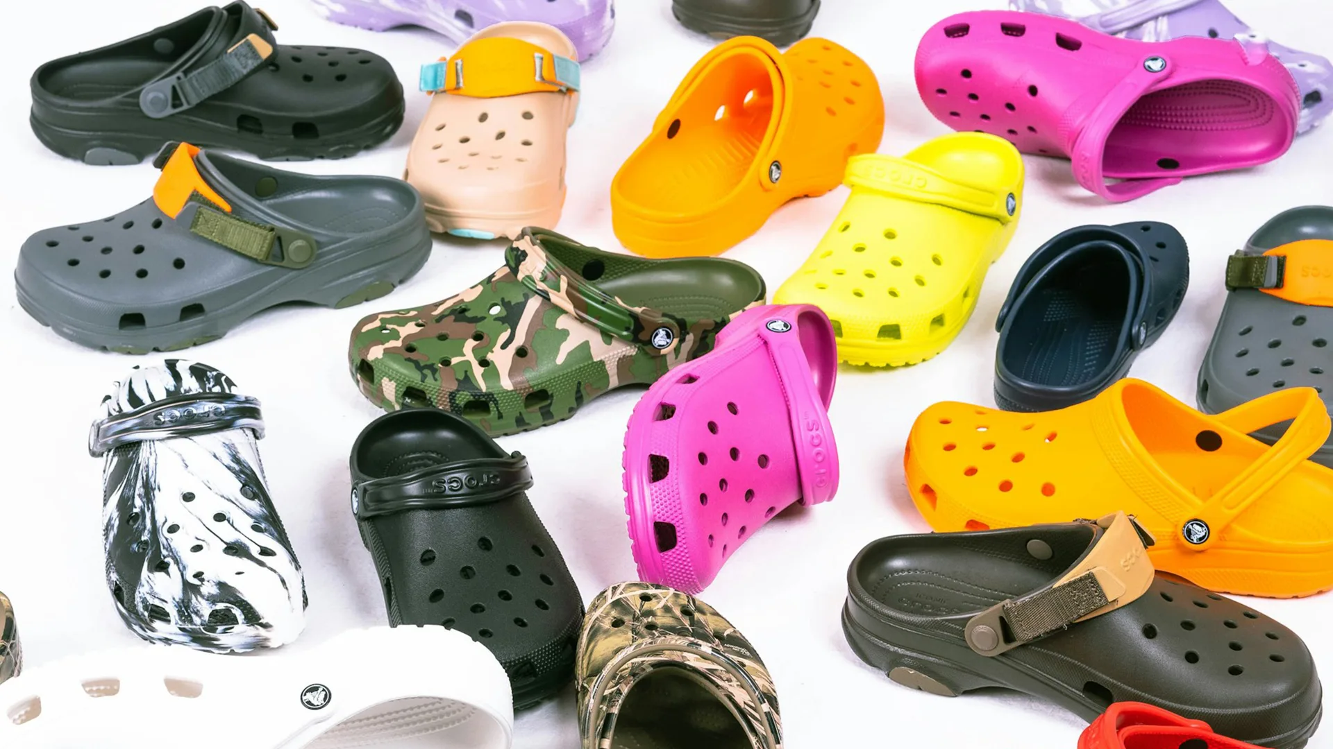 Many different coloured pairs of crocs on a white background