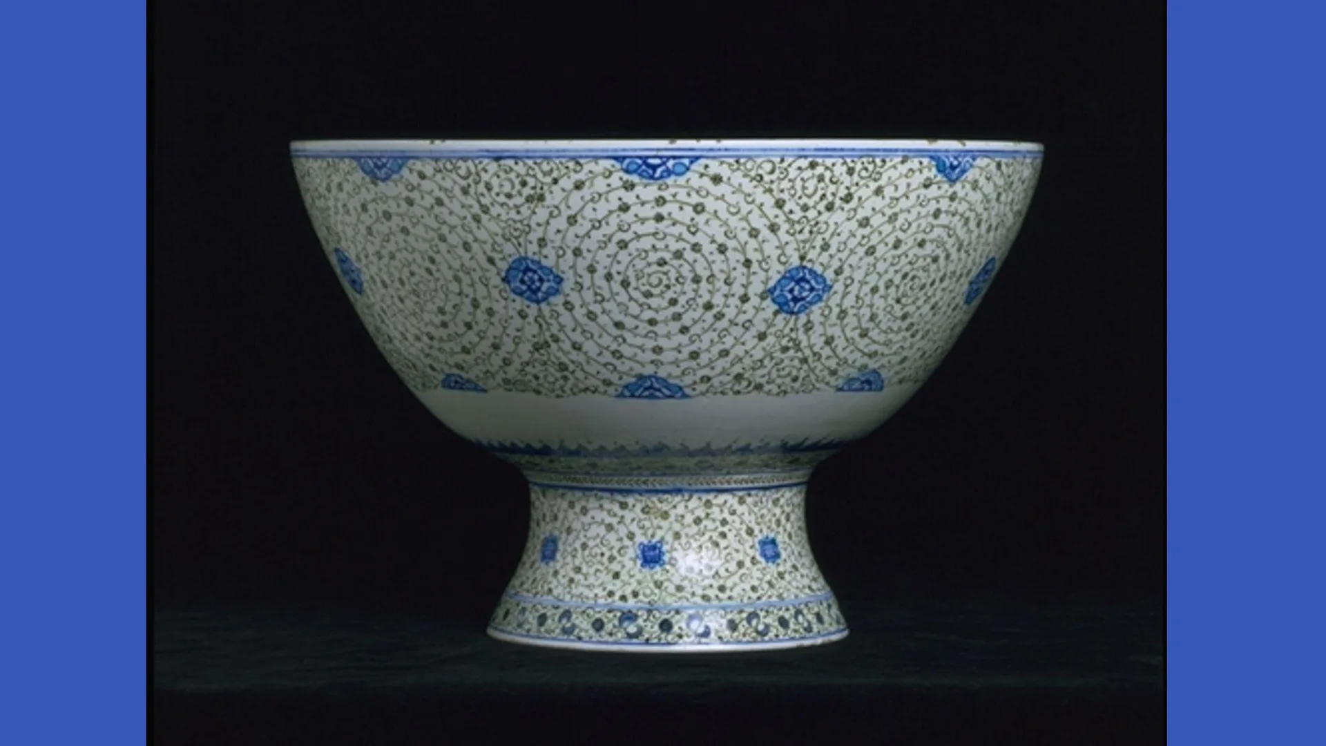A photograph of a porcelain blue and white bowl with painted decorations against a black background with blue borders