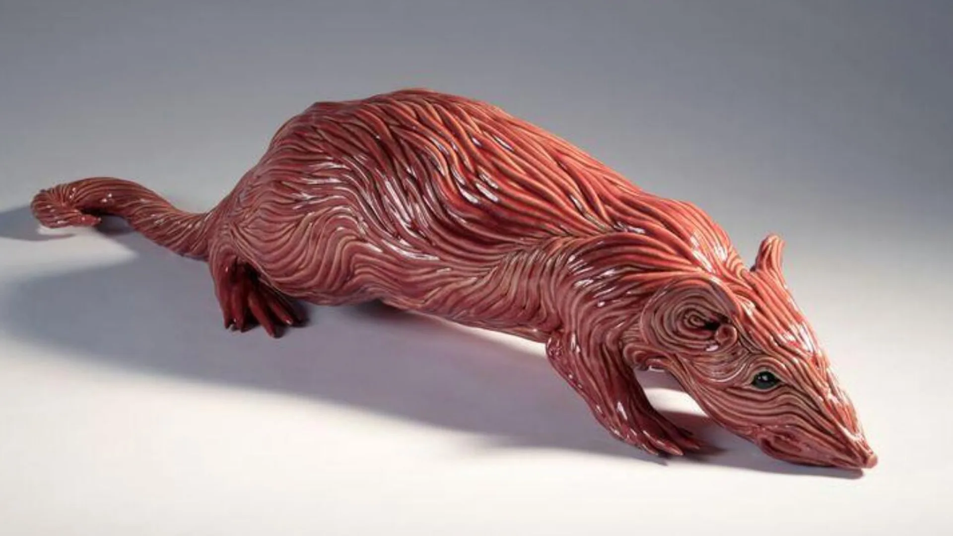 A photo of a V&A object of a ceramic rat with a red glaze on a white background