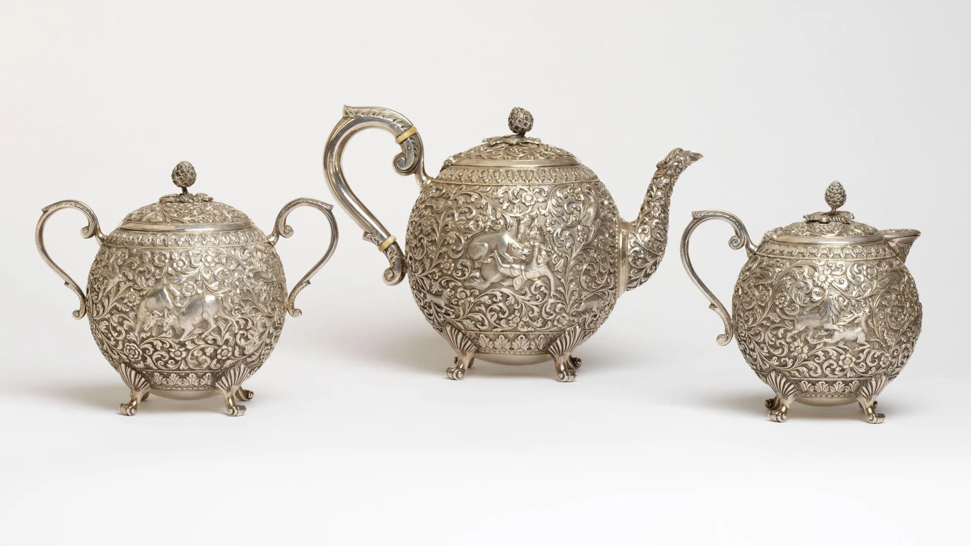A photograph of a kutch silver teapot and sugar bowl set of three, against a white background