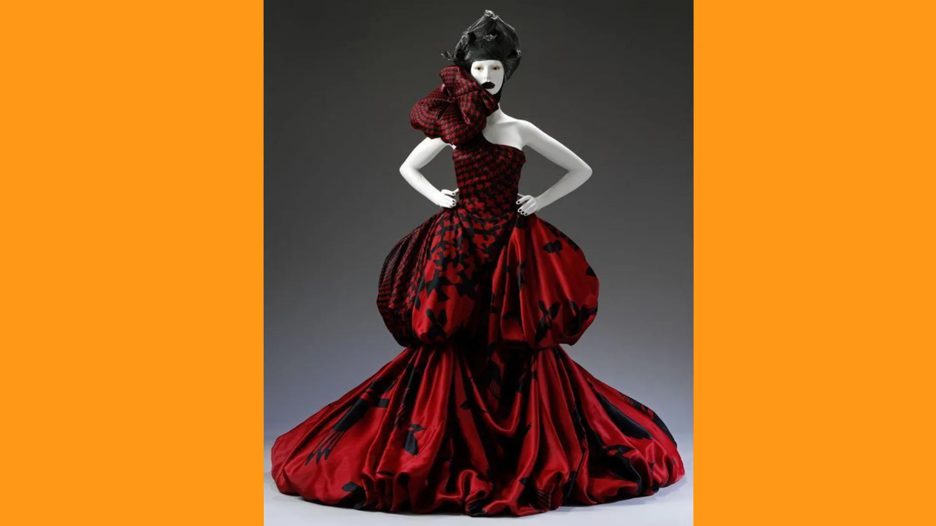 A photograph of a bubble shaped red dress designed by Alexander McQueen with a giant rose on the neck against a grey background with orange borders