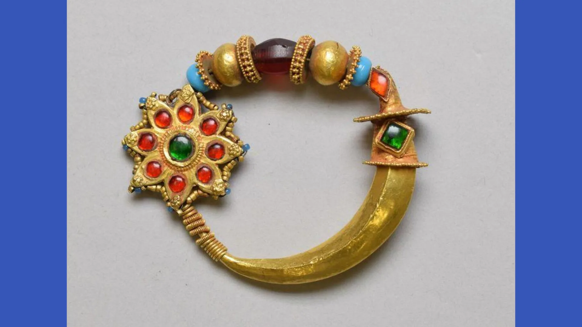 A photograph of a gold nose ring endorned with multi-coloured stones and beads against a grey background