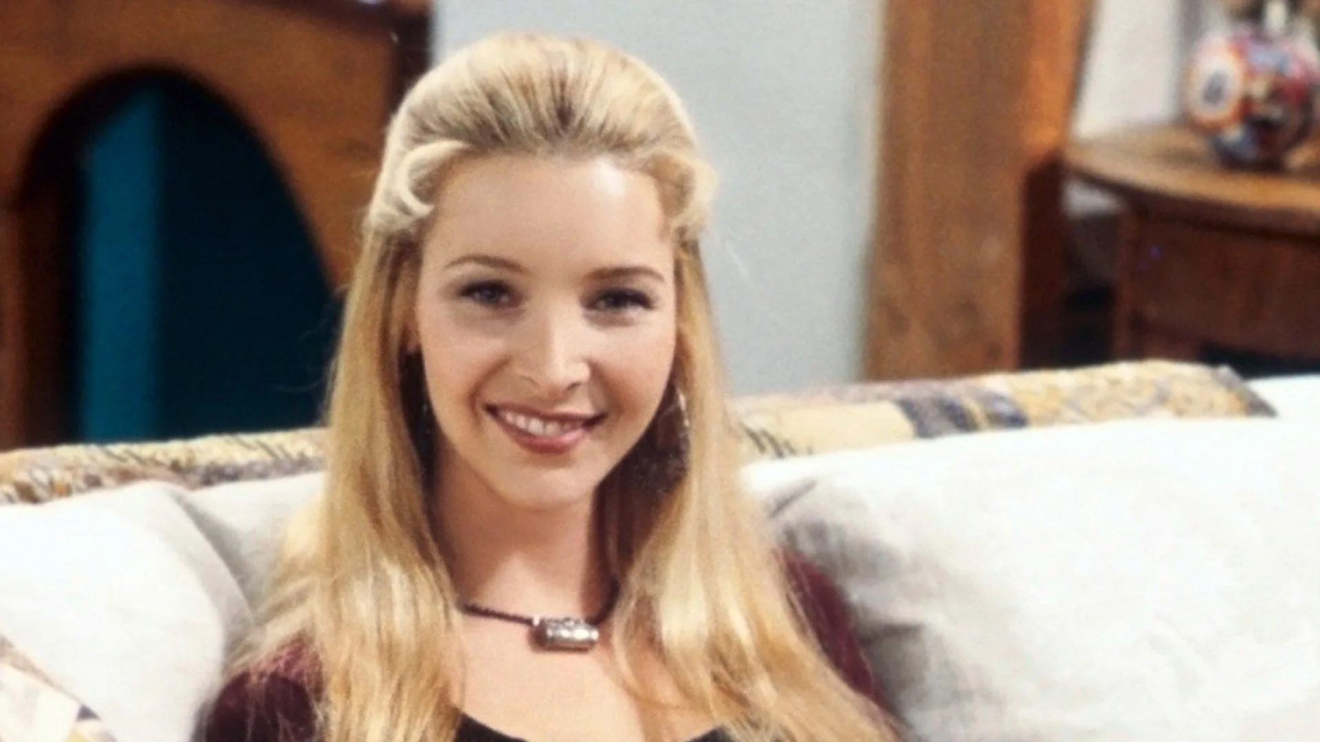 A photograph of Phoebe from Friends smiling at the camera sat on a white sofa