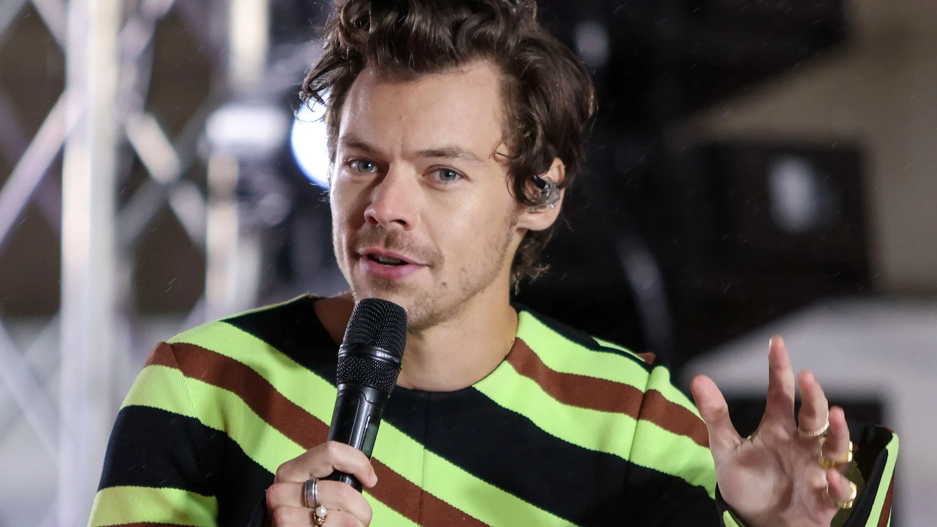 A photograph of singer Harry Styles holding a mic wearing a green and black striped shirt