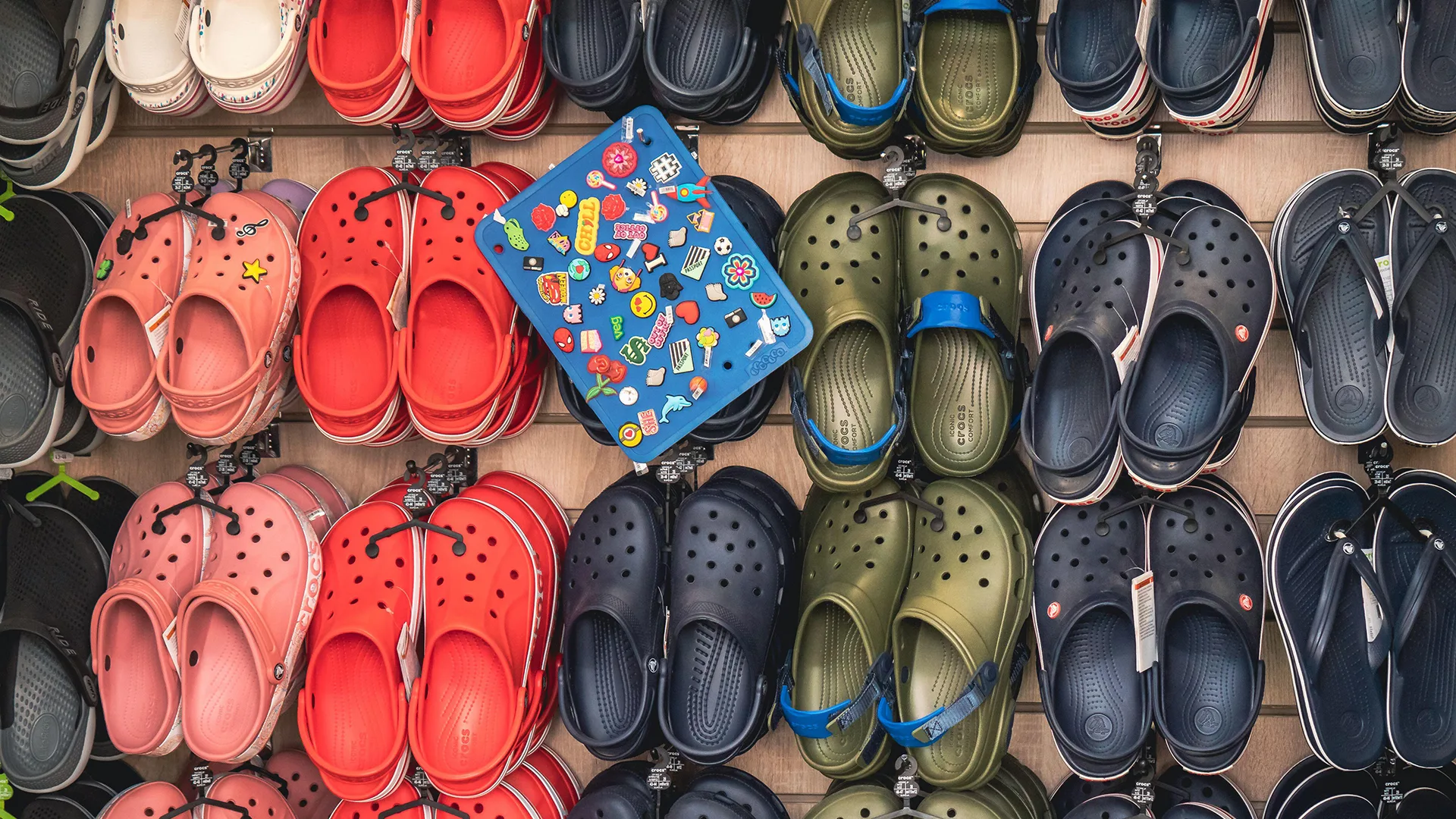Selection of green, navy and red crocs hung up on a wall in a shop 