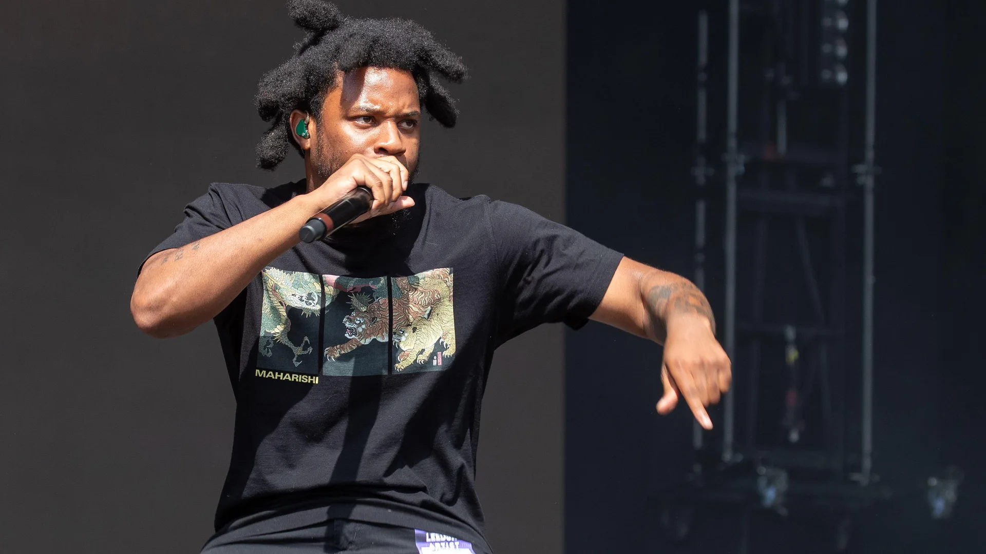 A photograph of Denzel Curry signing on stage with a mic against a black background