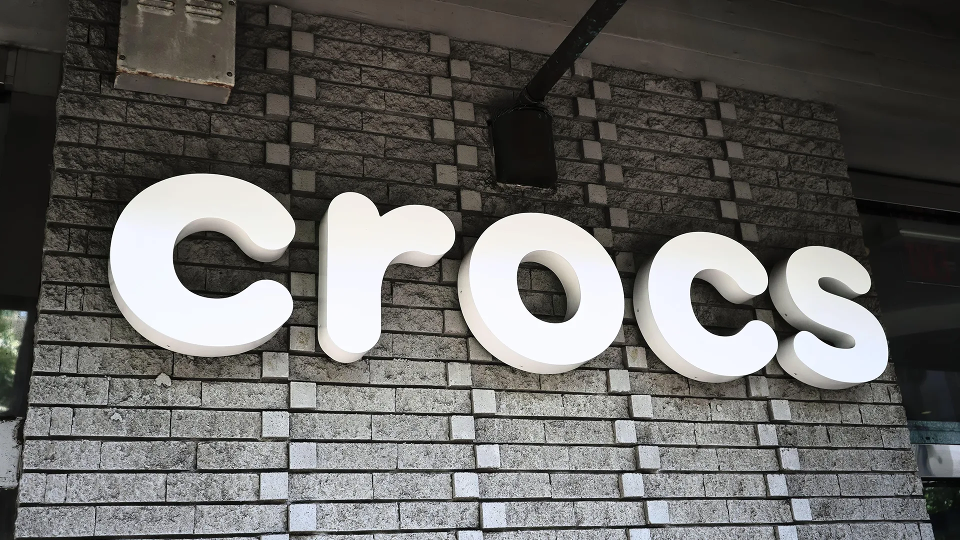 Crocs sign taken from outside a store. Written in white on a dark grey background