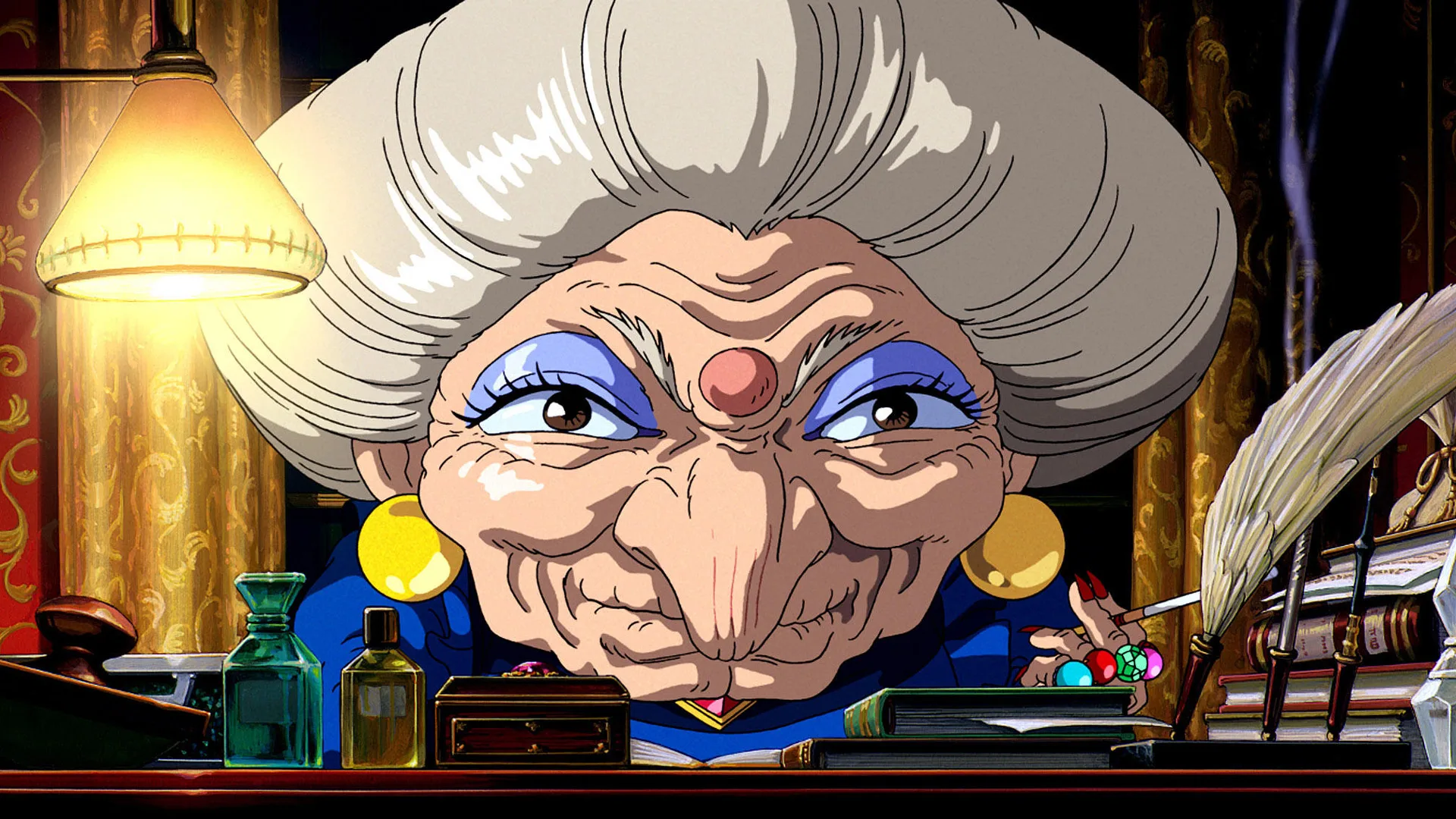 A still from the film Spirited Away showing a close up of the character Yubaba smiling directly at the camera with a light beside her and books in front of her