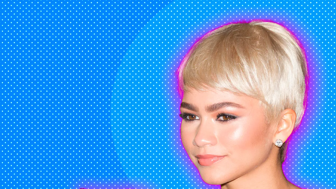 A photograph of Zendaya in a blonde wig smiling against a blue dotted background with a pink halo