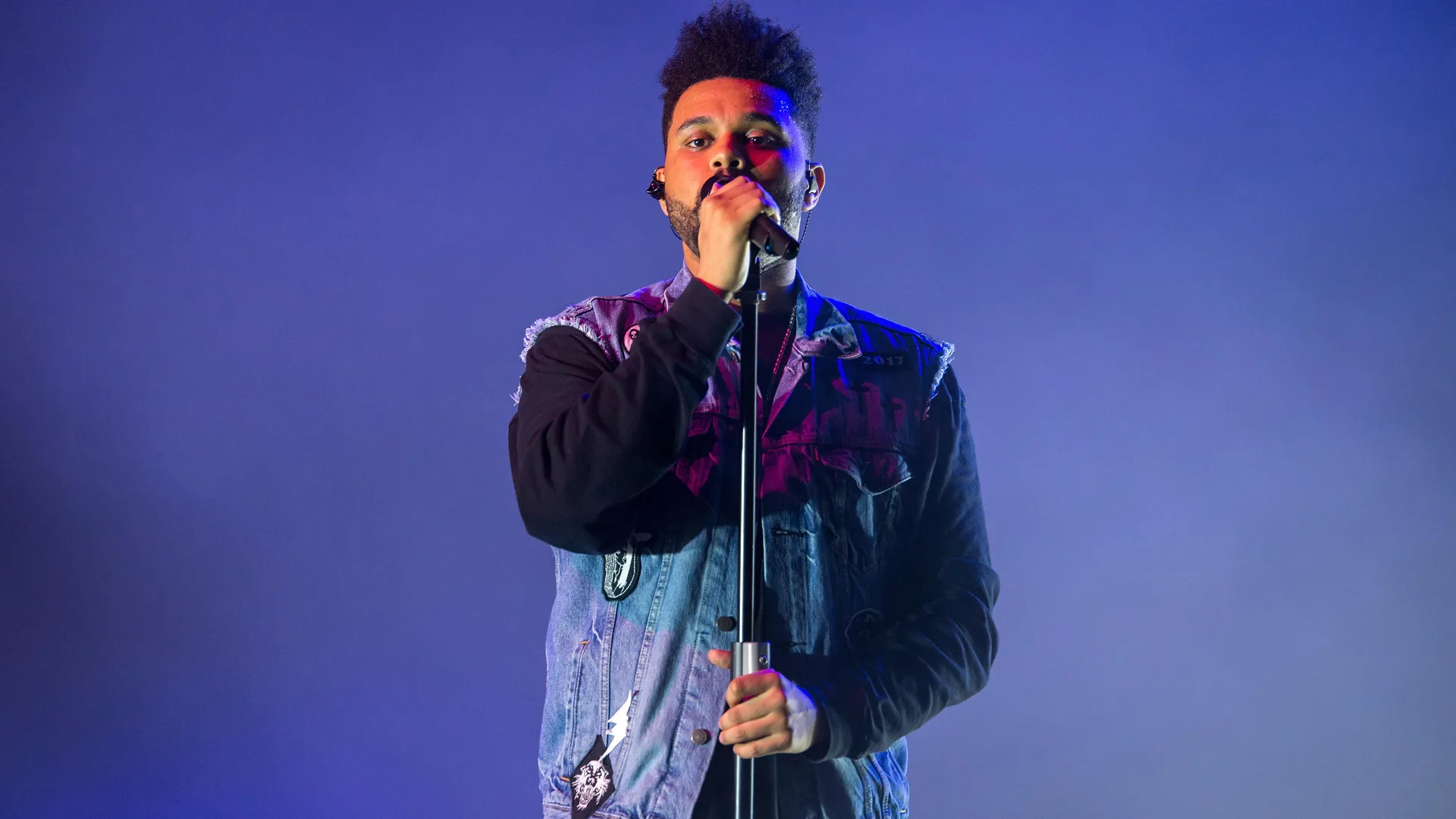 A photograph of the singer from The Weeknd holding the mic against a blue background