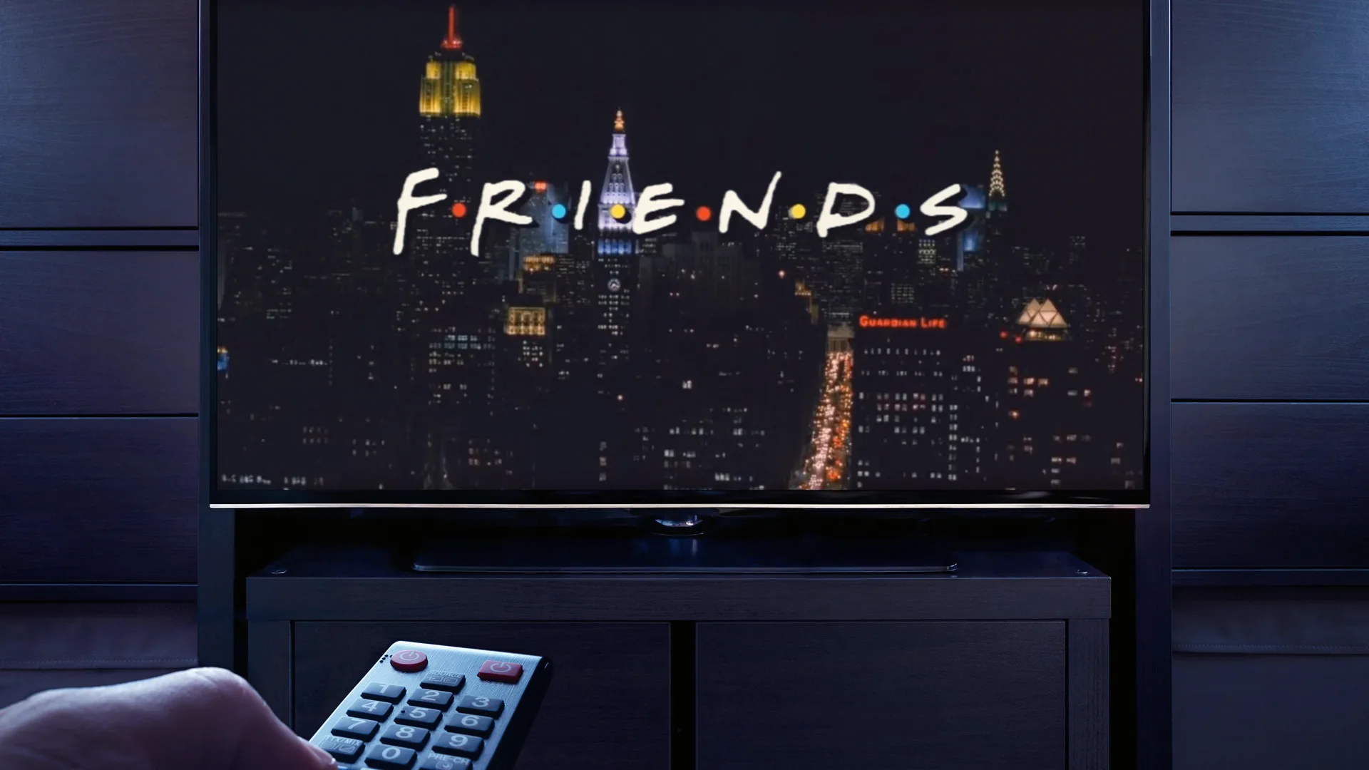 A photograph of a TV screen showing the intro of Friends with someone pointing a remote control at the tv in the dark
