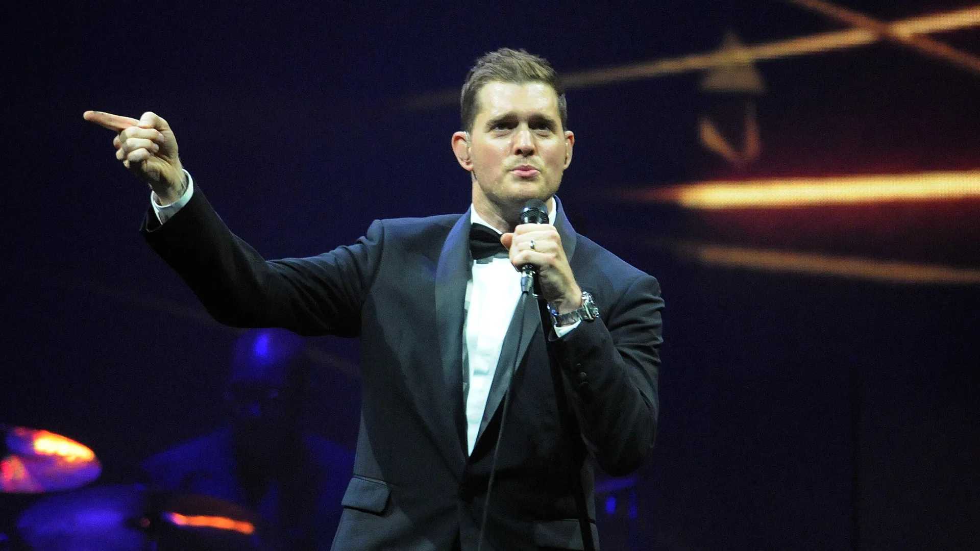A photograph of the singer Michael Buble wearing a tux with a mic performing on stage