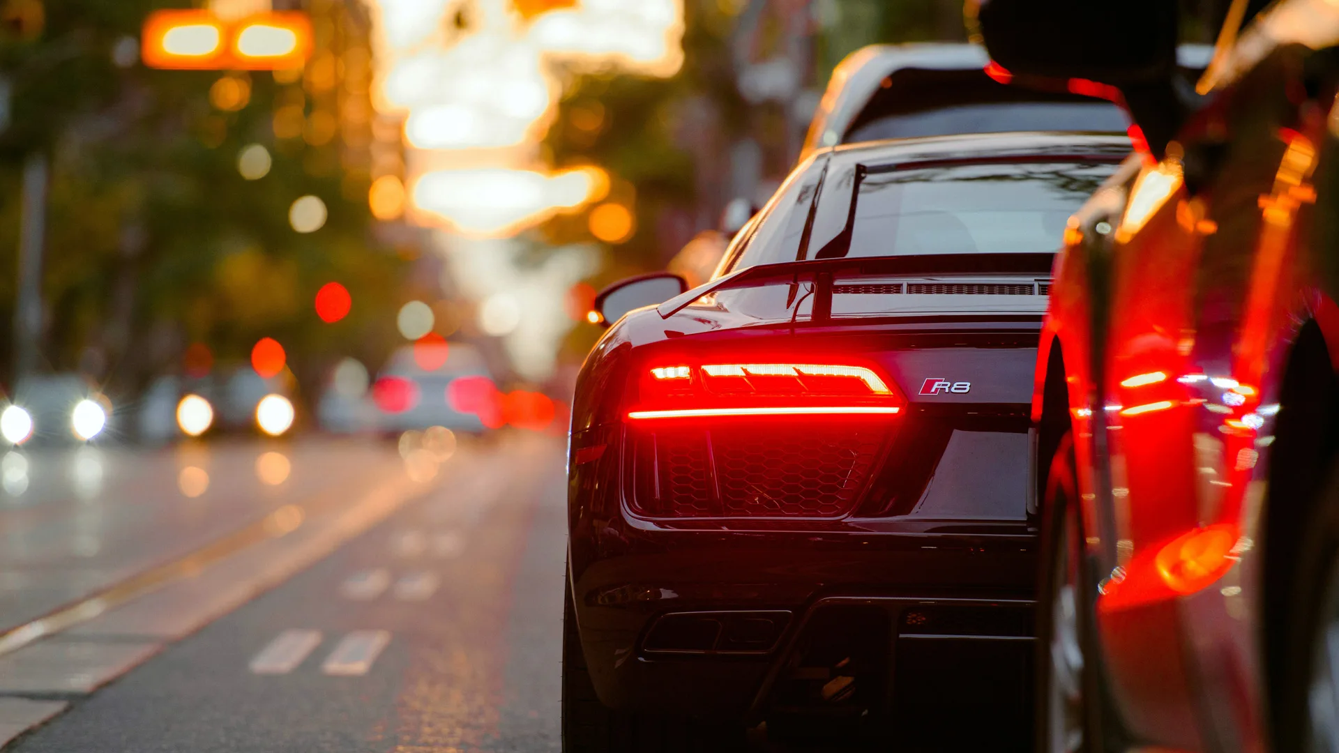 A photograph of the back of a sports car with the red brake lights on against a blurred shot of the road with car lights