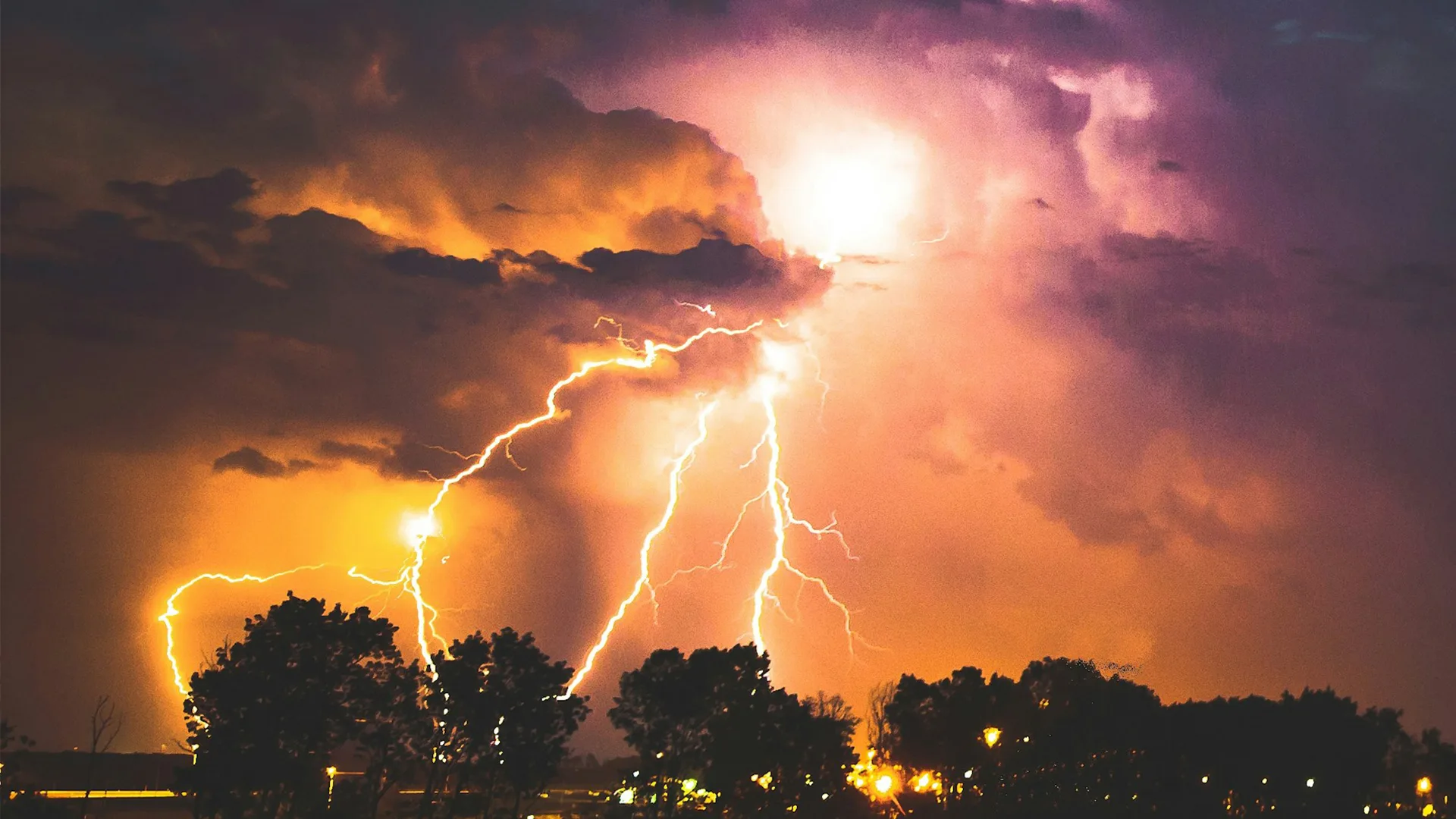 Lightning striking at night which makes the clouds appear purple and orange