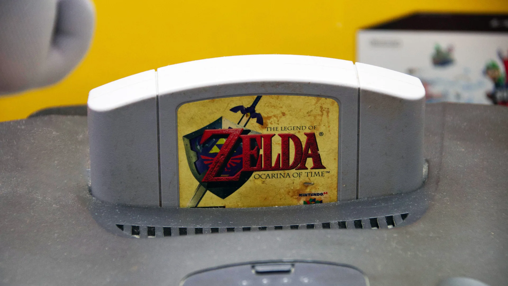 A photo of a Zelda game cartridge in a grey games console set against a yellow background.