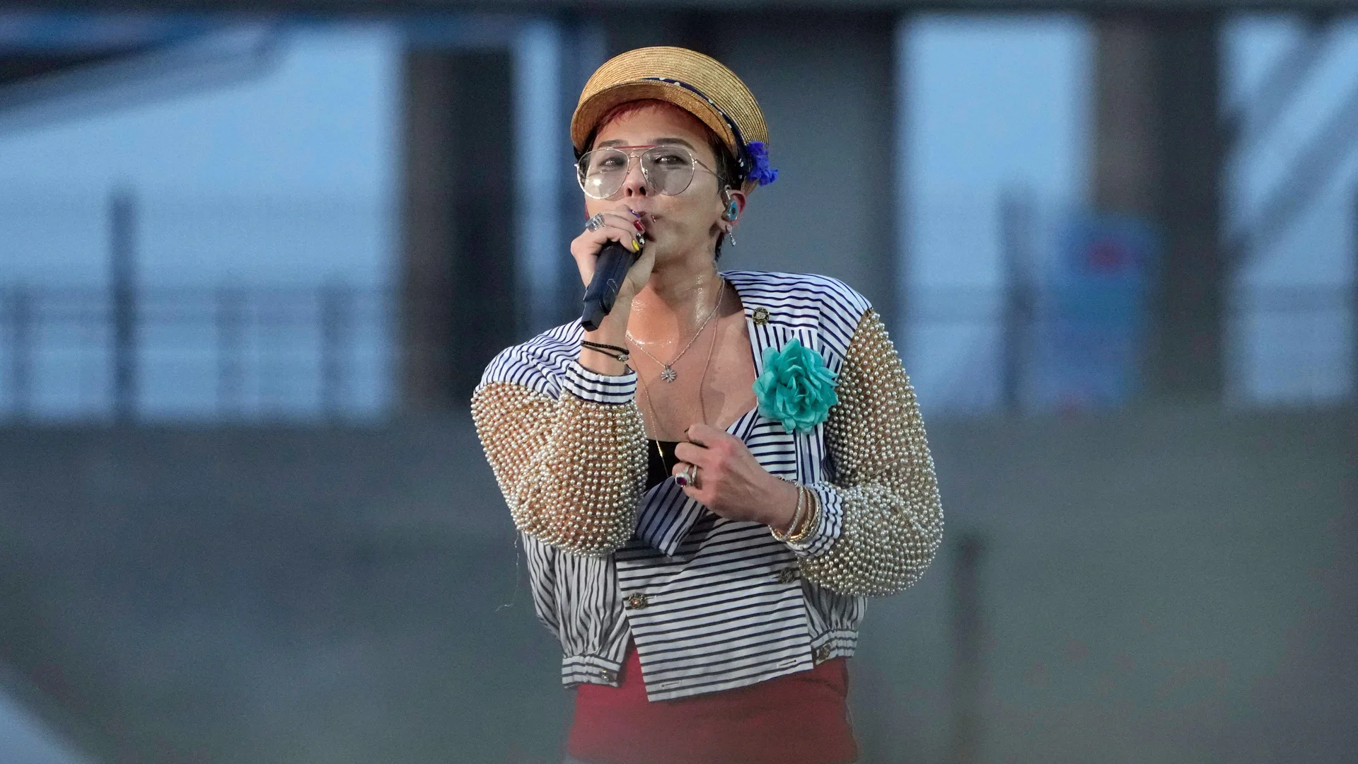 The singer Gdragon from the band BIGBANG singing on stage into a mic wearing a striped top and beige flatcap.