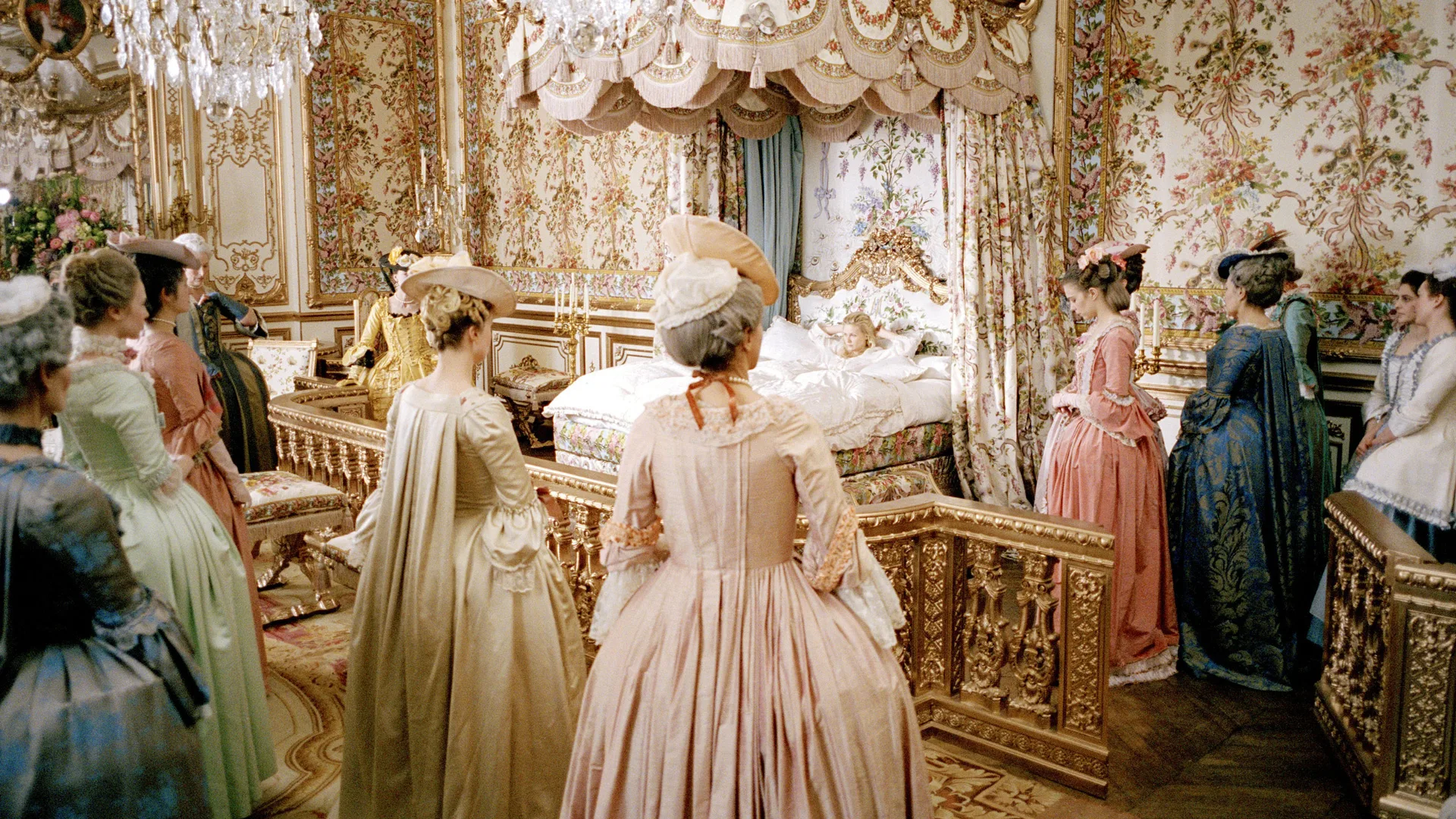 A still from the Sofia Coppola move Marie Antoinette (2006) showing Kirsten Dunst as Marie Antoinette sat in bed surrounded by her ladies in waiting.