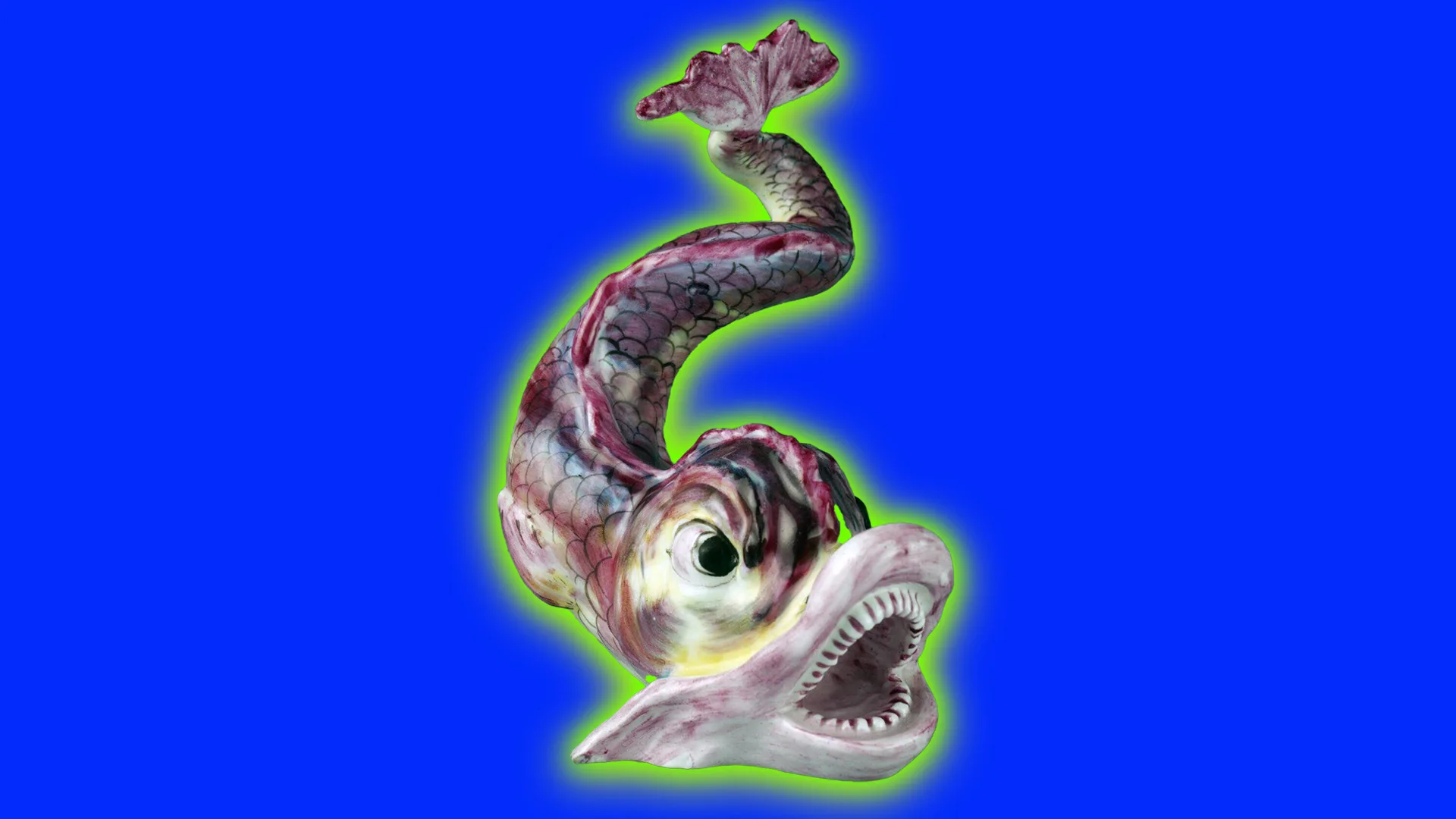 An image of a porcelain figure in the shape of a dolphin / fish. It has a scary look on it's face and is bearing it's teeth with it's tail in the air. It is set against a cobalt blue background and a green halo.