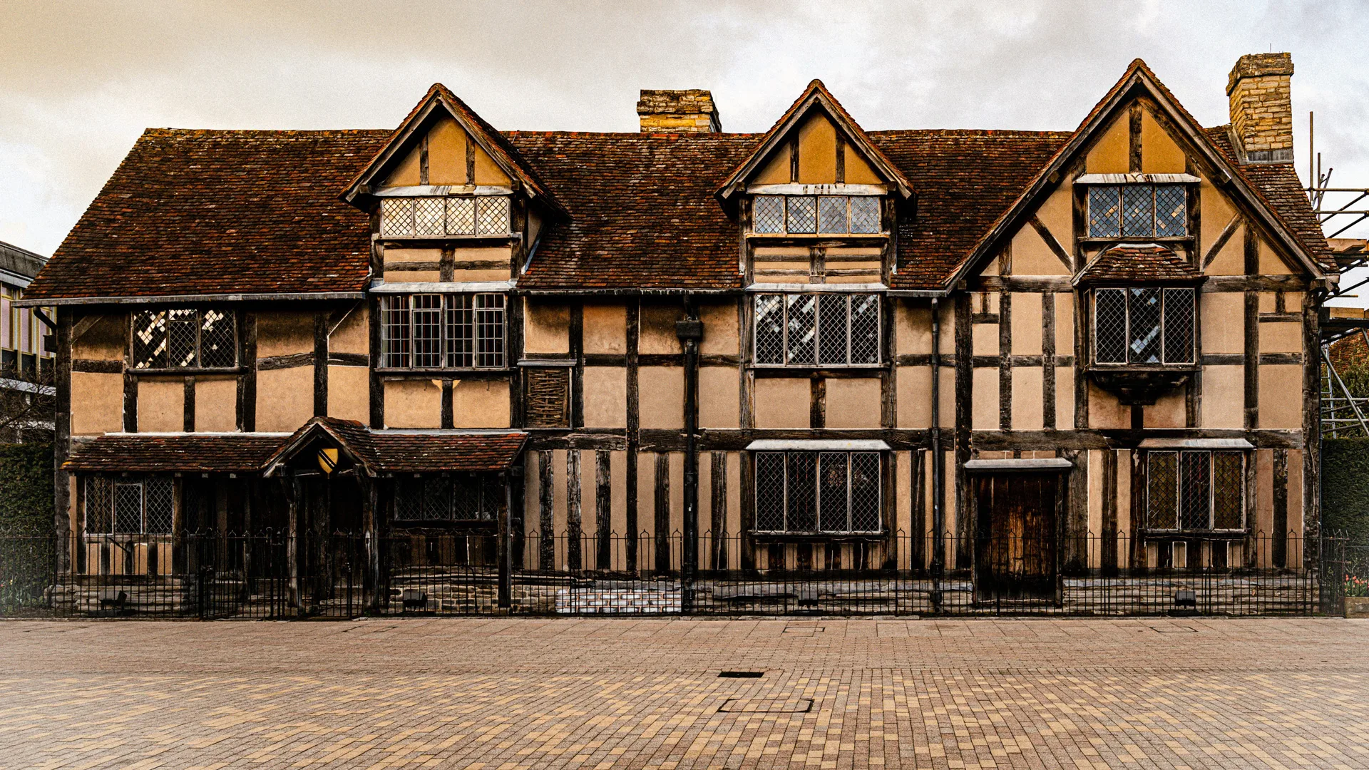 A photo showing the English town of Stratford Upon Avon with a tudor house in brown and white set against a grey cloudy sky,