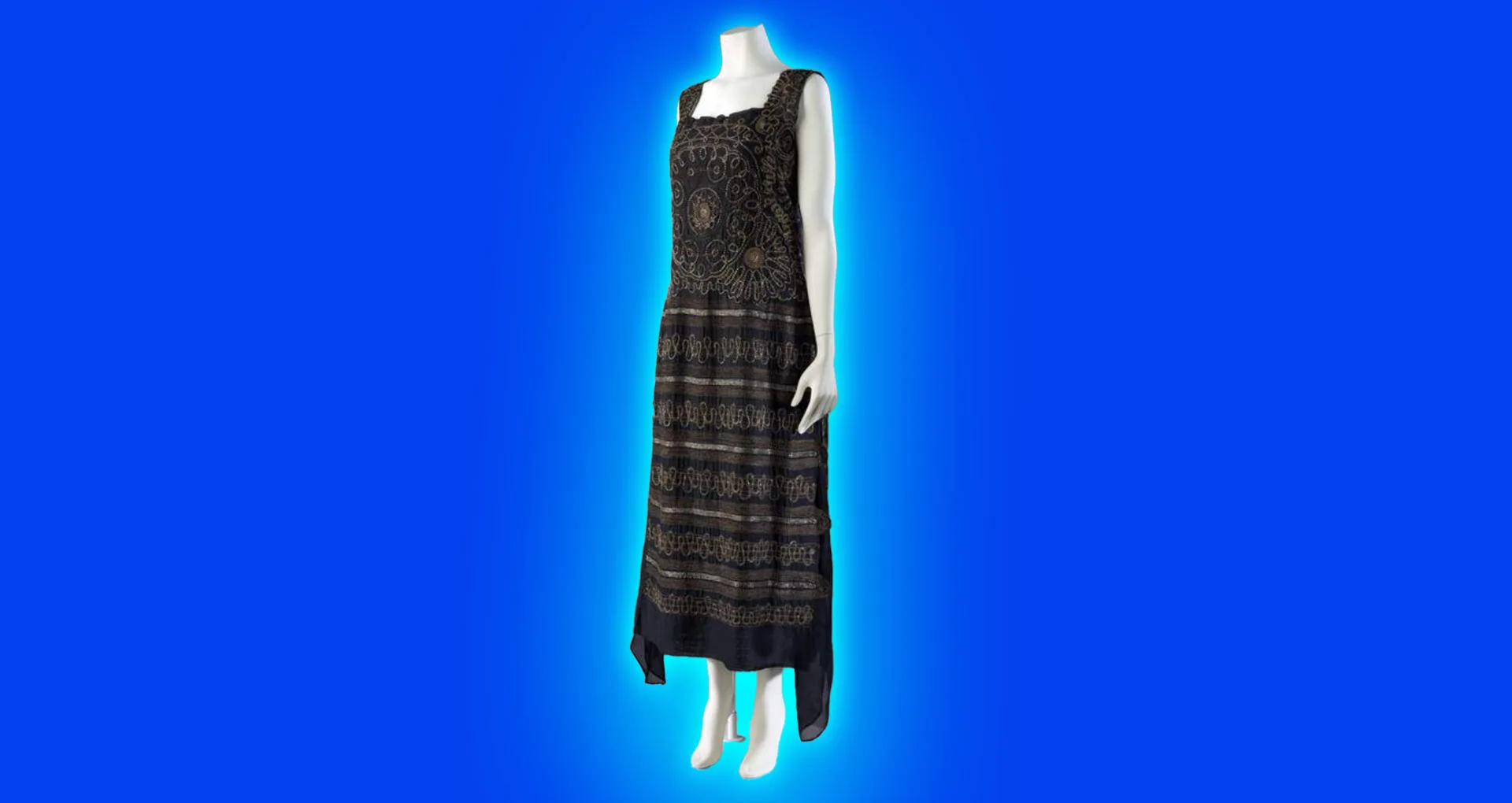 An image of a black 1920s dress designed by Coco Chanel on a white mannequin against a blue background with a light blue halo.