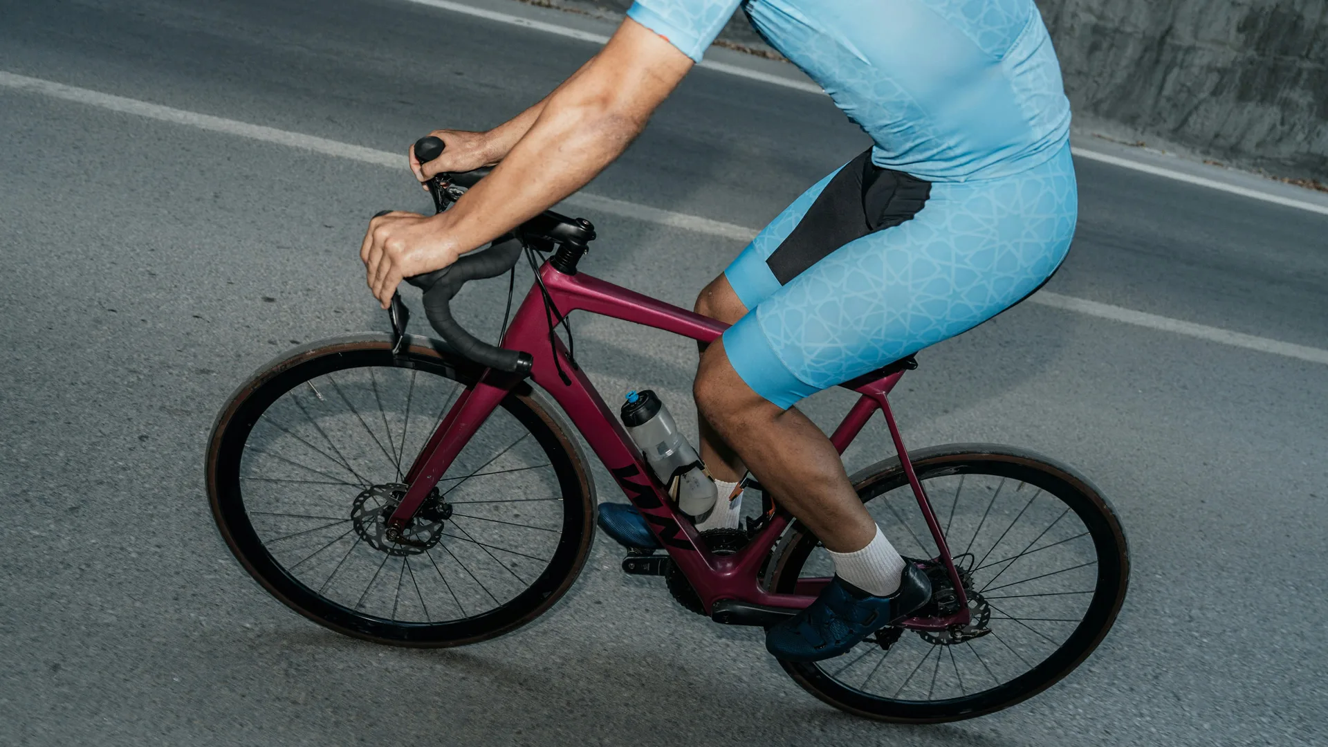 A photo of a cyclist riding a bike wearing light blue cycling shorts and top on a road.