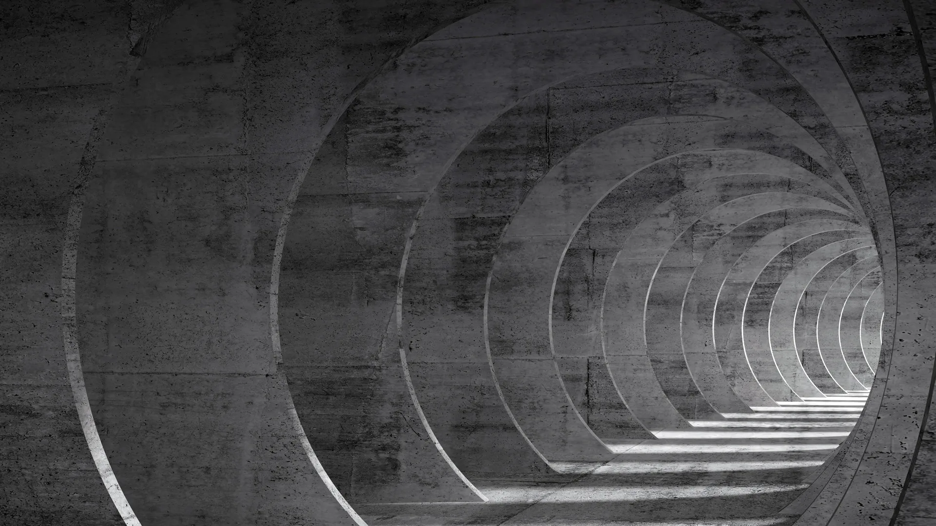 A photo of a tunnel with circular archways creating the tunnel in grey with light at the smaller end of the tunnel.