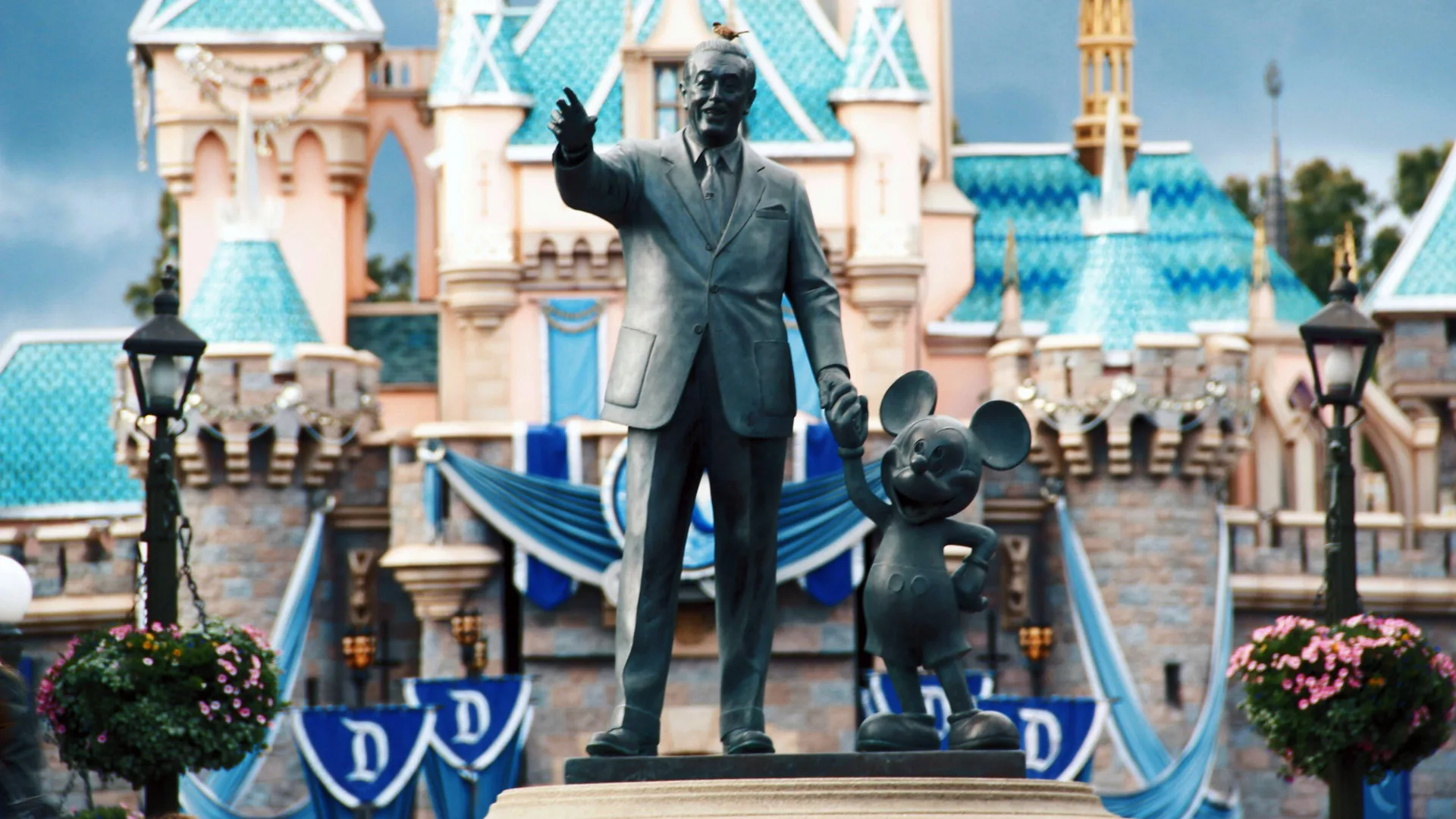 A photo from Disneyland showing a statue of Walt Disney and Mickey Mouse holding hands stood outside the Cinderella castle.