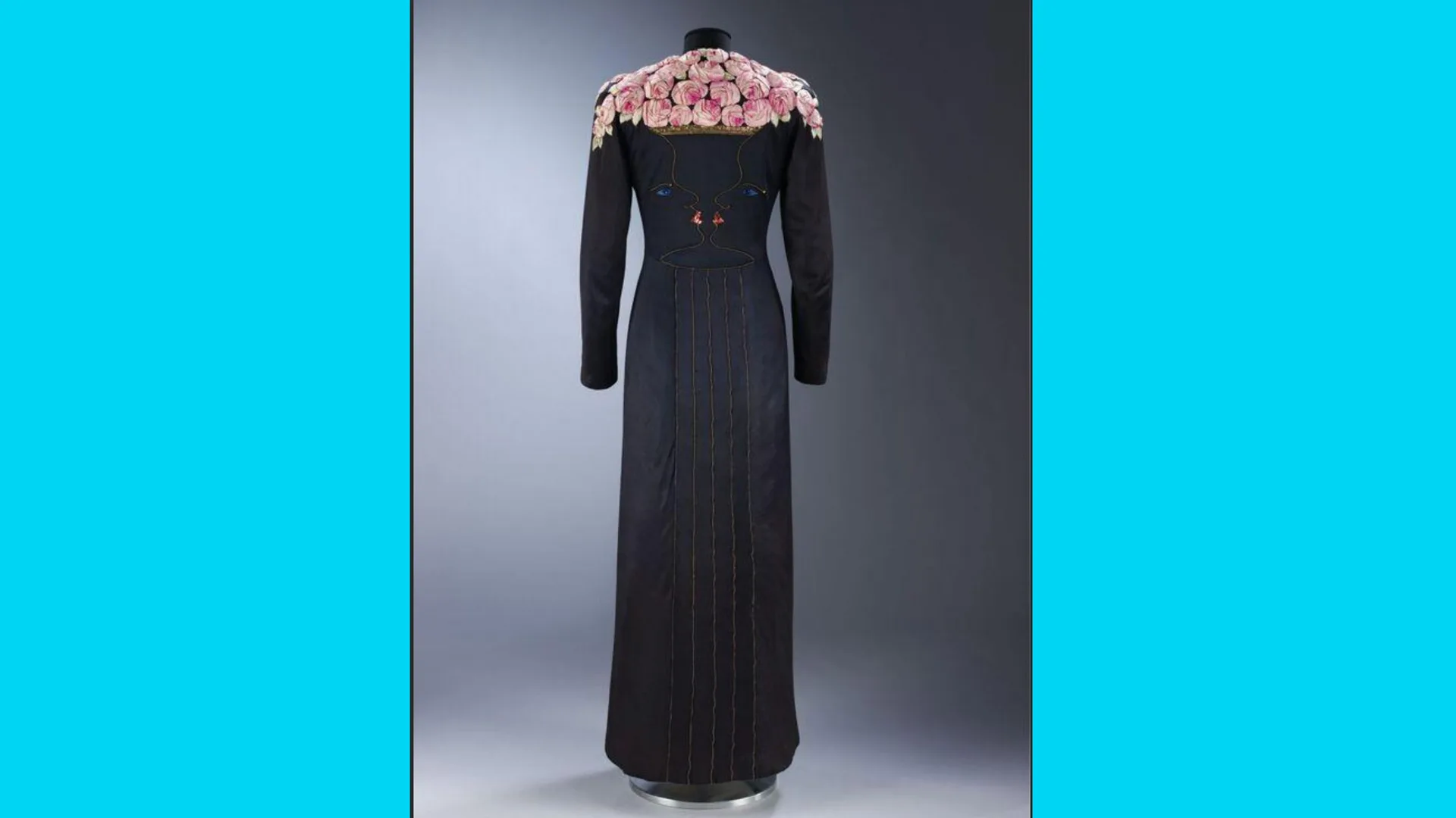 A photo of an evening coat by Elsa Schiaparelli (1937), embroidered by Jean Cocteau showing a vase holding roses on the shoulders formed by two faces in profile. It is bordered with blue either side.