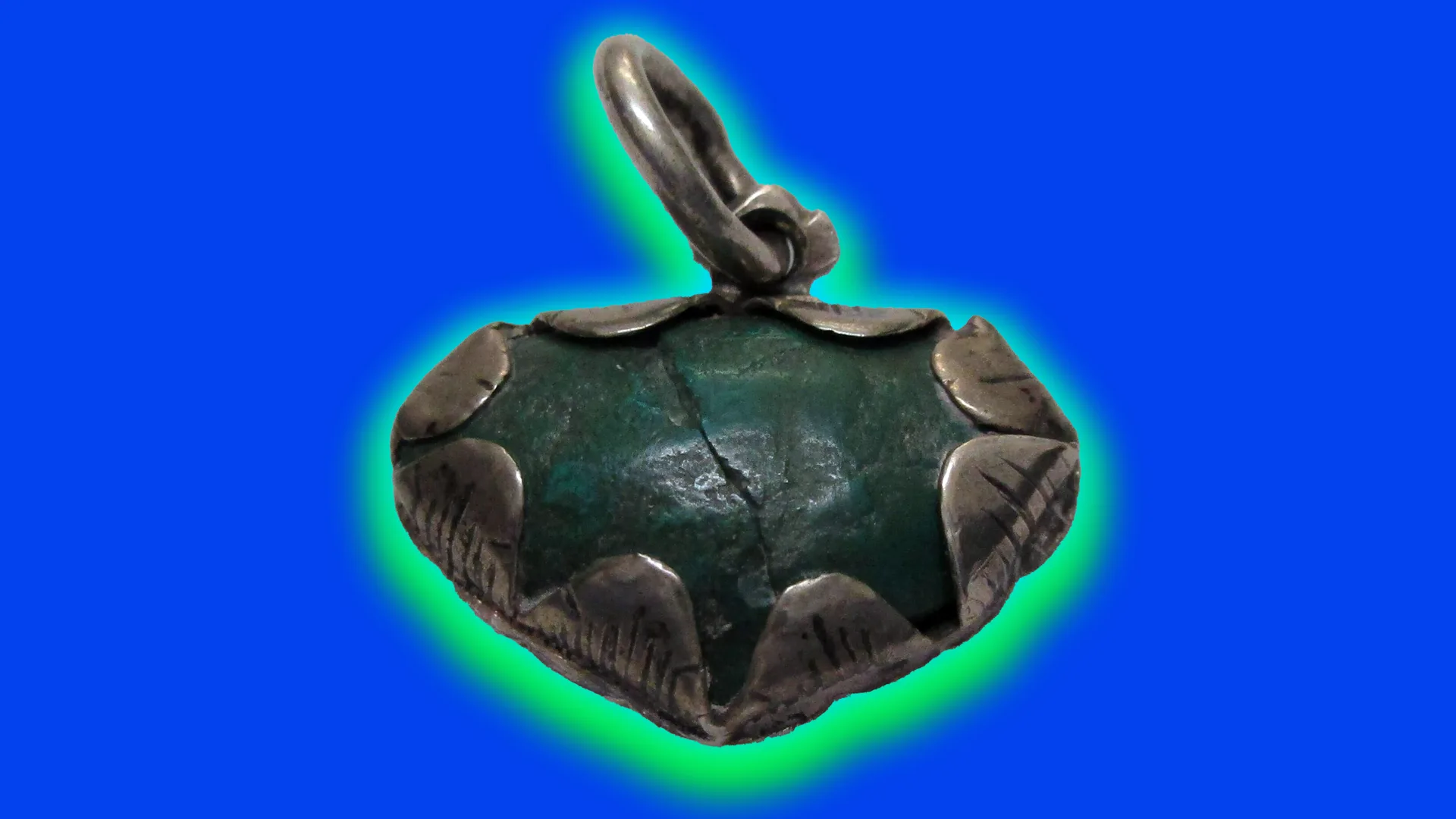 A photo of a 1700s green heart shaped amulet with a brass setting and loop at the top. It is set against a blue background with a green halo.