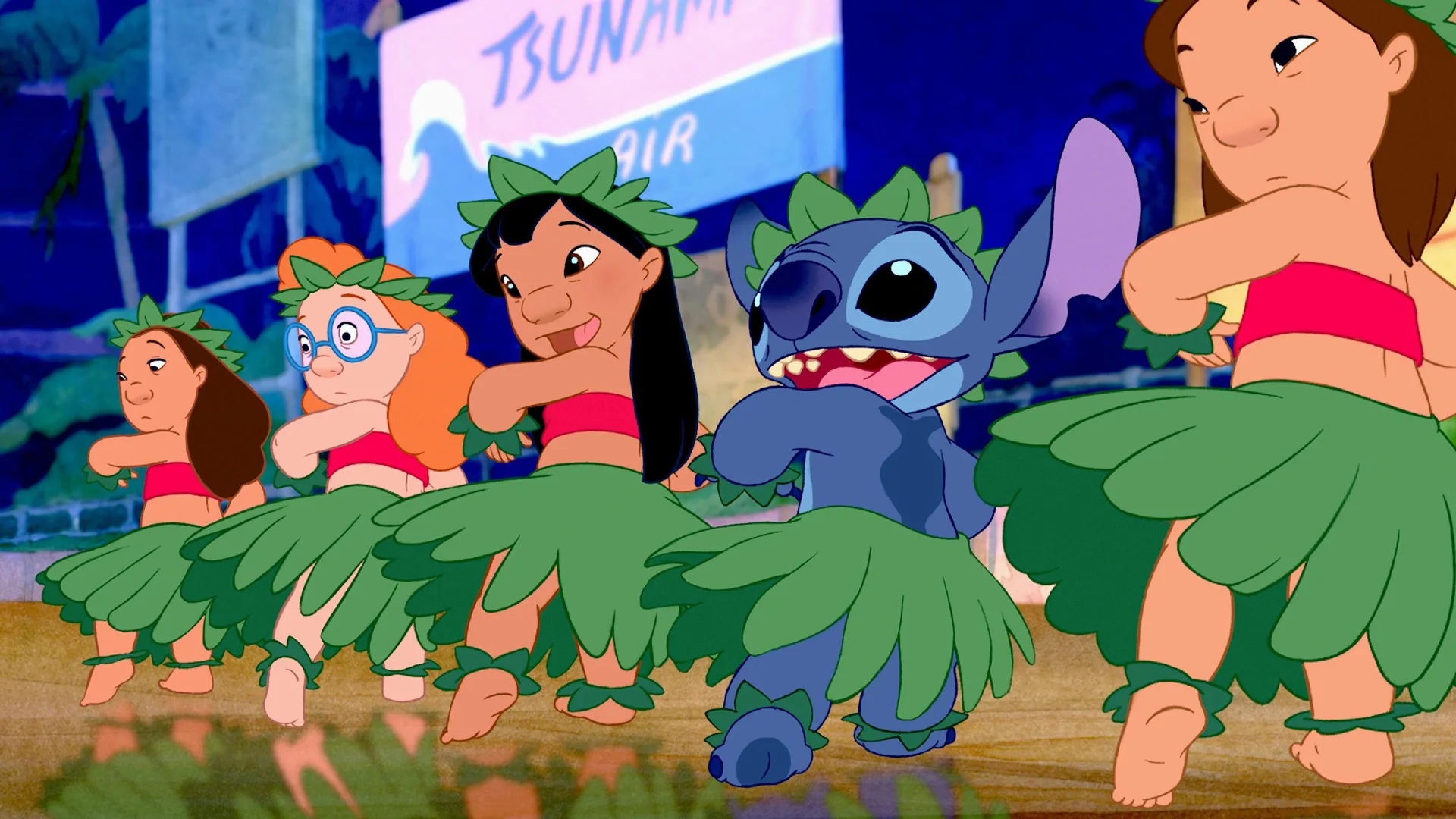 A still from Lilo and Stitch (2002) showing Lilo and Stitch dancing on stage with other dancers wearing hula skirts and haircrowns made from foliage against a sign in pink and blue.