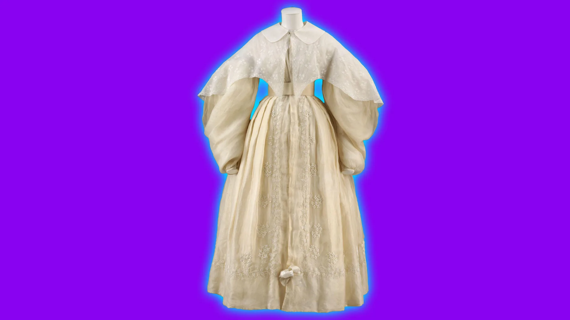 A wedding dress from 1834 showing exagerrated puffed sleeves and high neck in ivory cream with a floral embroidered pattern on the skirt. It is set against a purple background with a blue halo.