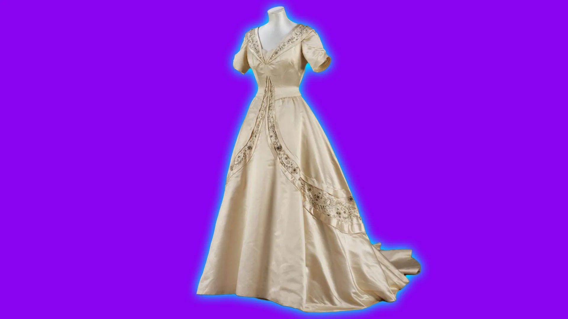 A silk ivory 1950s wedding gown designed by Norman Hartnell. The gown has a deep v neck with embroidery and sweeping band of embroidery on the skirt. It is set against a purple background with a blue halo.