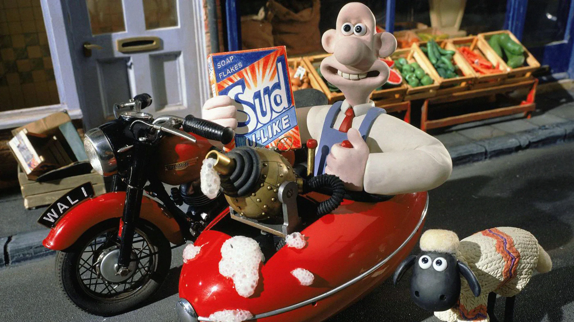 A still from Wallace and Gromit A Close Shave showing Wallace holding a box of suds sat in his motorcycle with Shaun the Sheep stood next to him outside a grocery shop.