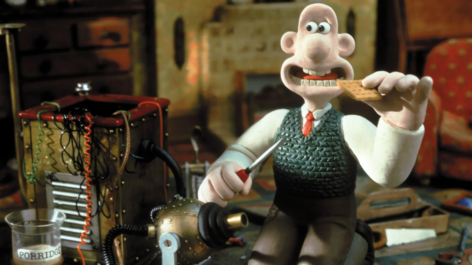 A still from Wallace and Gromit A Close Shave showing Wallace about to eat a cracker surrounded by food looking at a machine he's invented whilst holding a screwdriver.