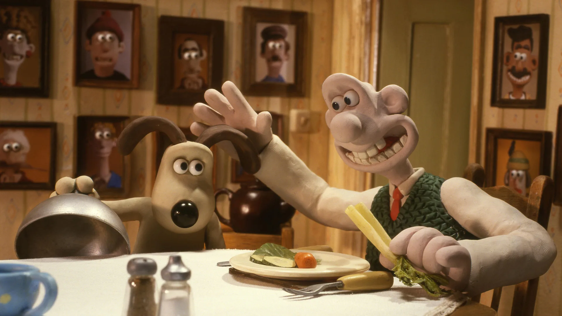 A still from Wallace and Gromit The Curse of the Were-Rabbit showing Gromit about to pat Gromit on the head as they sit at the dinner table.