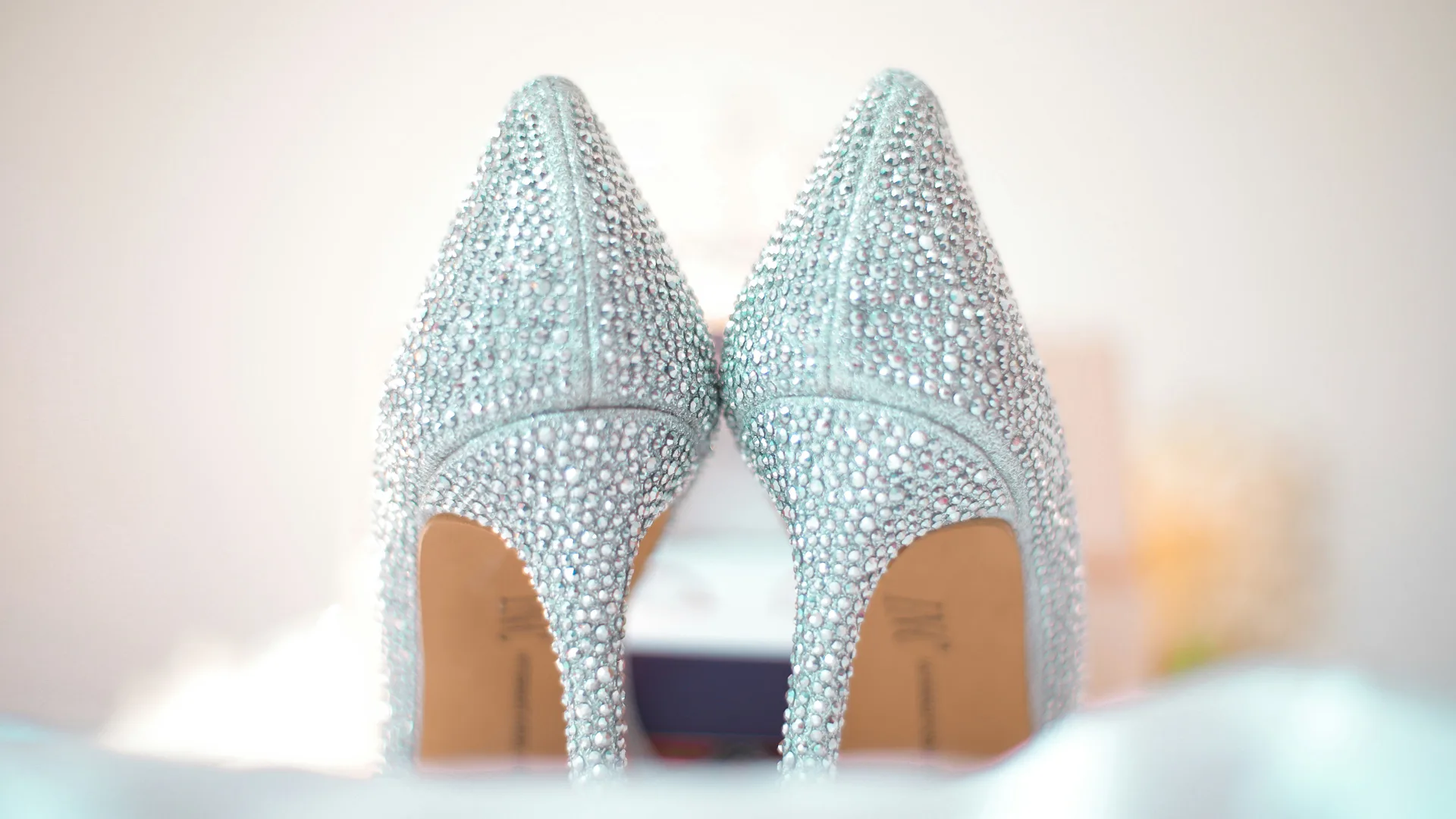 A photo of a pair of silver shoes shown from the back with the heels partially obscured by an out of focus object in the foreground.