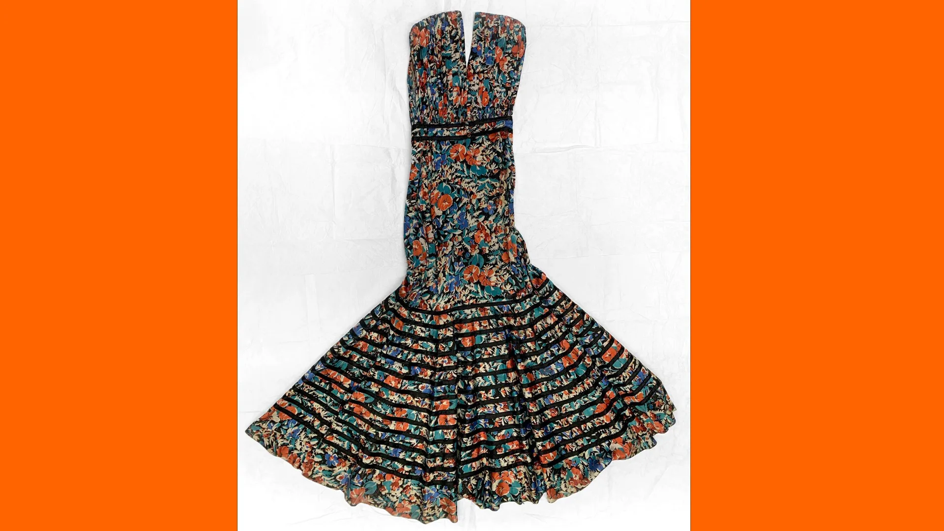 A photo of a 1930s satin dress with floral pattern and black satin binding on the skirt. It is set against a white background with orange borders either side.