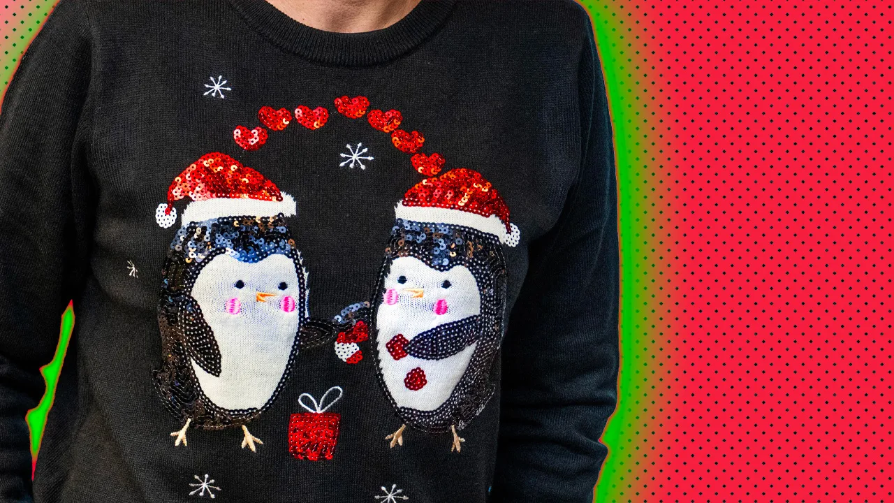 An image of a black christmas jumper with penguins on the front in little red christmas hats and hearts above their heads with a green halo and red dotted background.