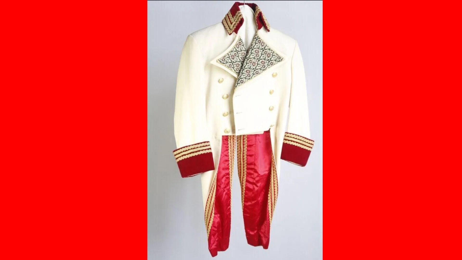 An image of a white jacket with large patterned lapels, gold buttons and red trimmed sleeves with red coattails hanging down against a grey background with red borders either side.