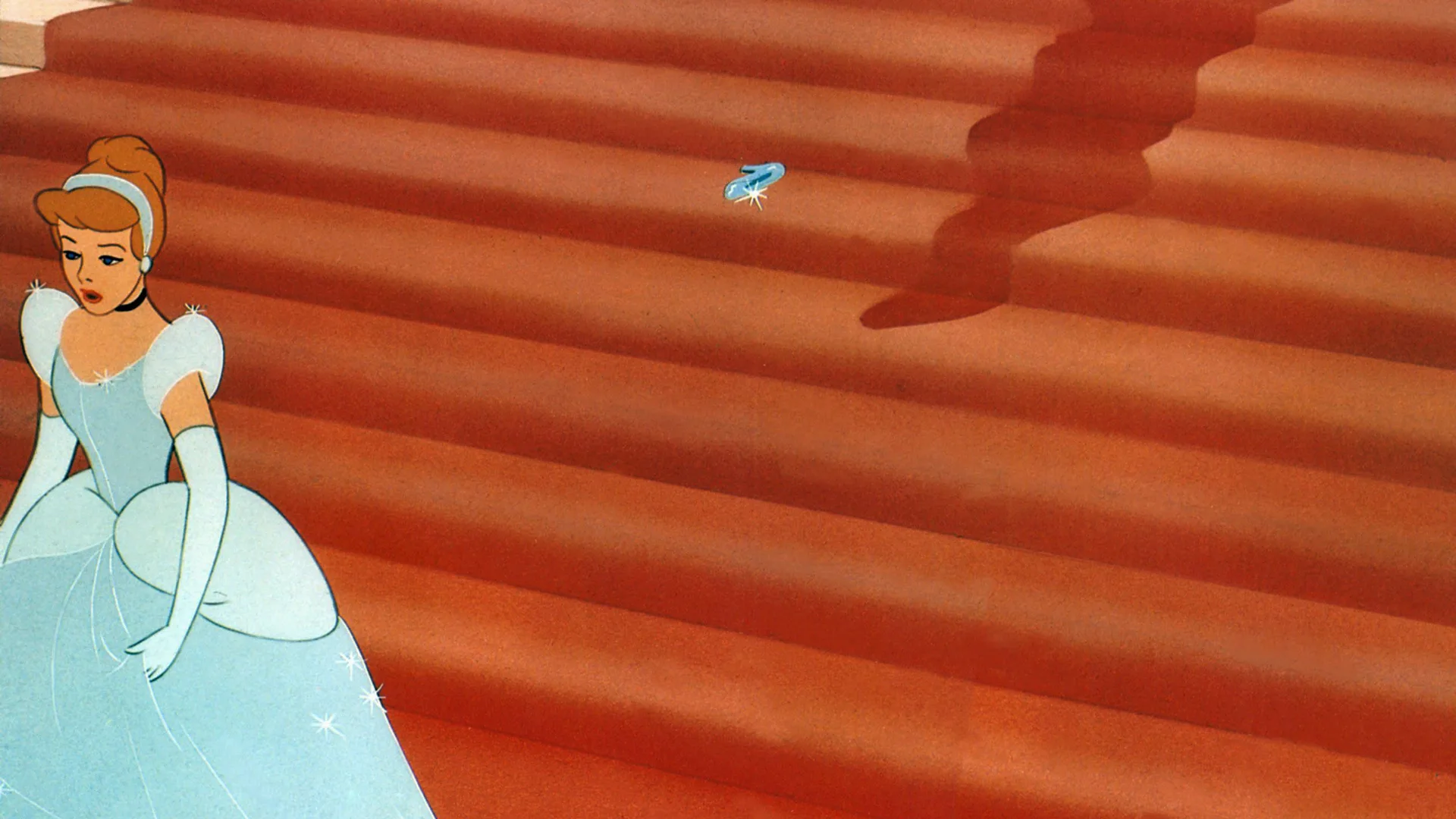 A still from Disney's Cinderella showing Cinderella running down the red stairs in her blue sparkly dress with a glass slipper left on the steps.