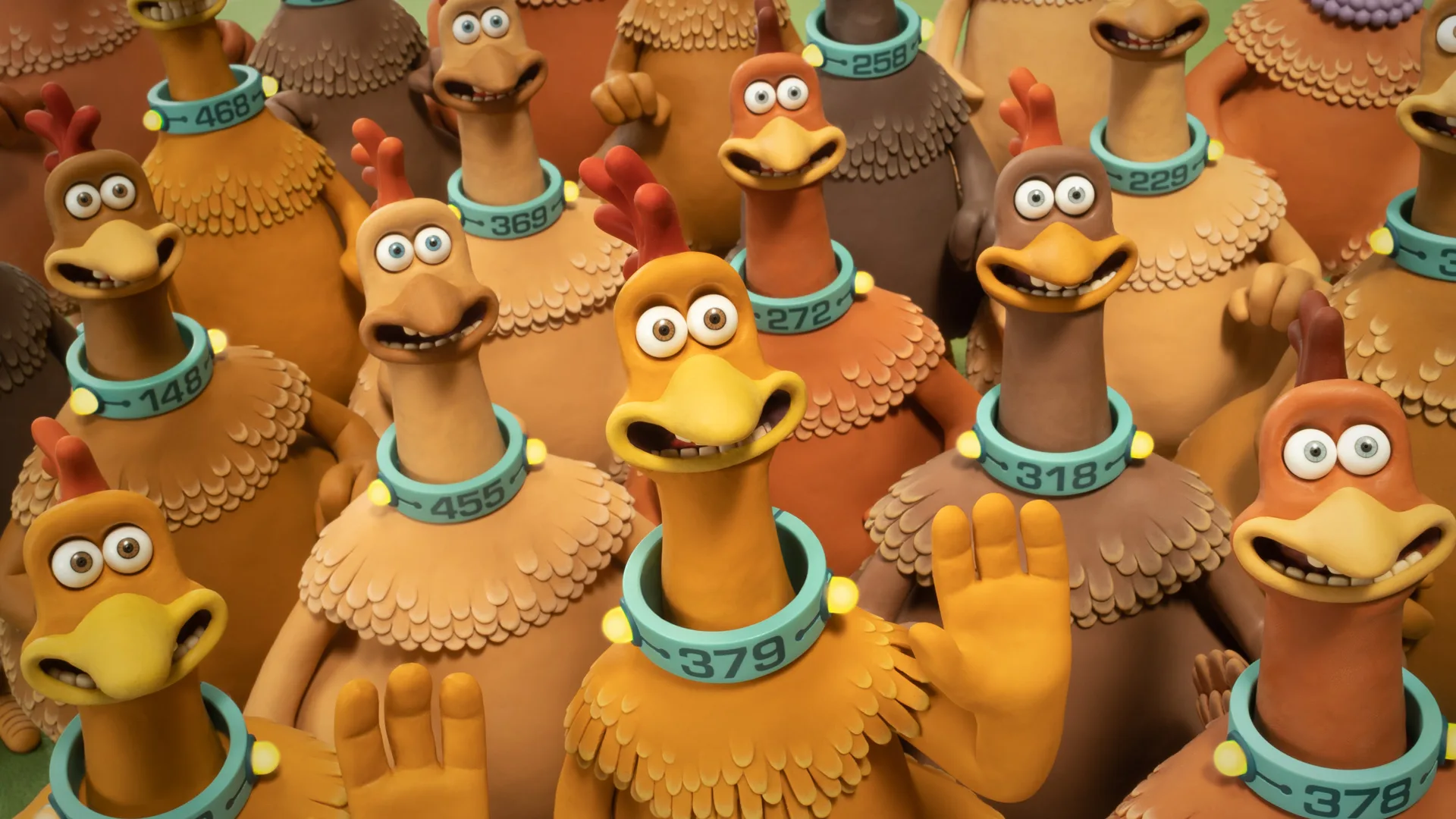 A still from Chicken Run showing a group of chickens stood together smiling and waving with blue collars around their necks.