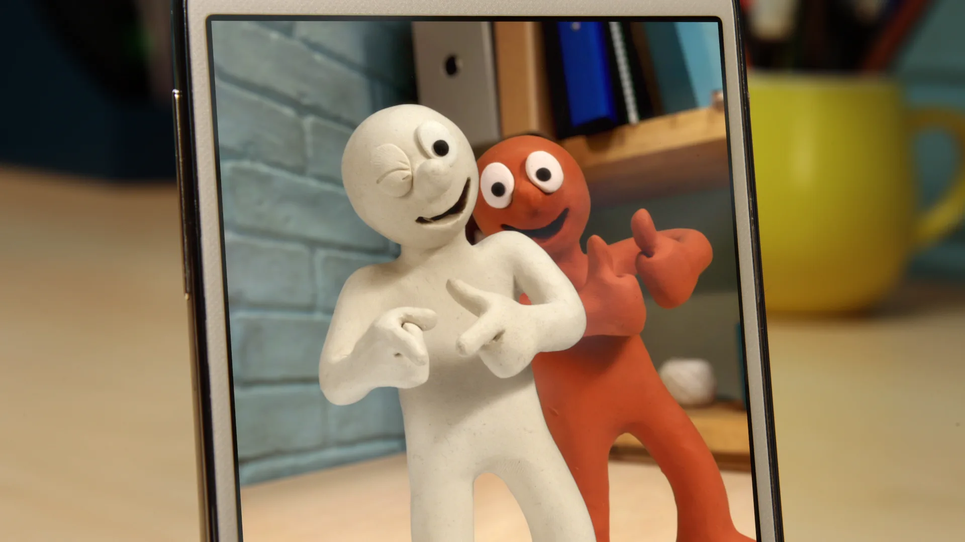 An image of Morph and Chas taking a selfie with Chas sticking his fingers toward the viewer with a wink and Morph behind him giving two thumbs up. They are in a room with a brick wall background.