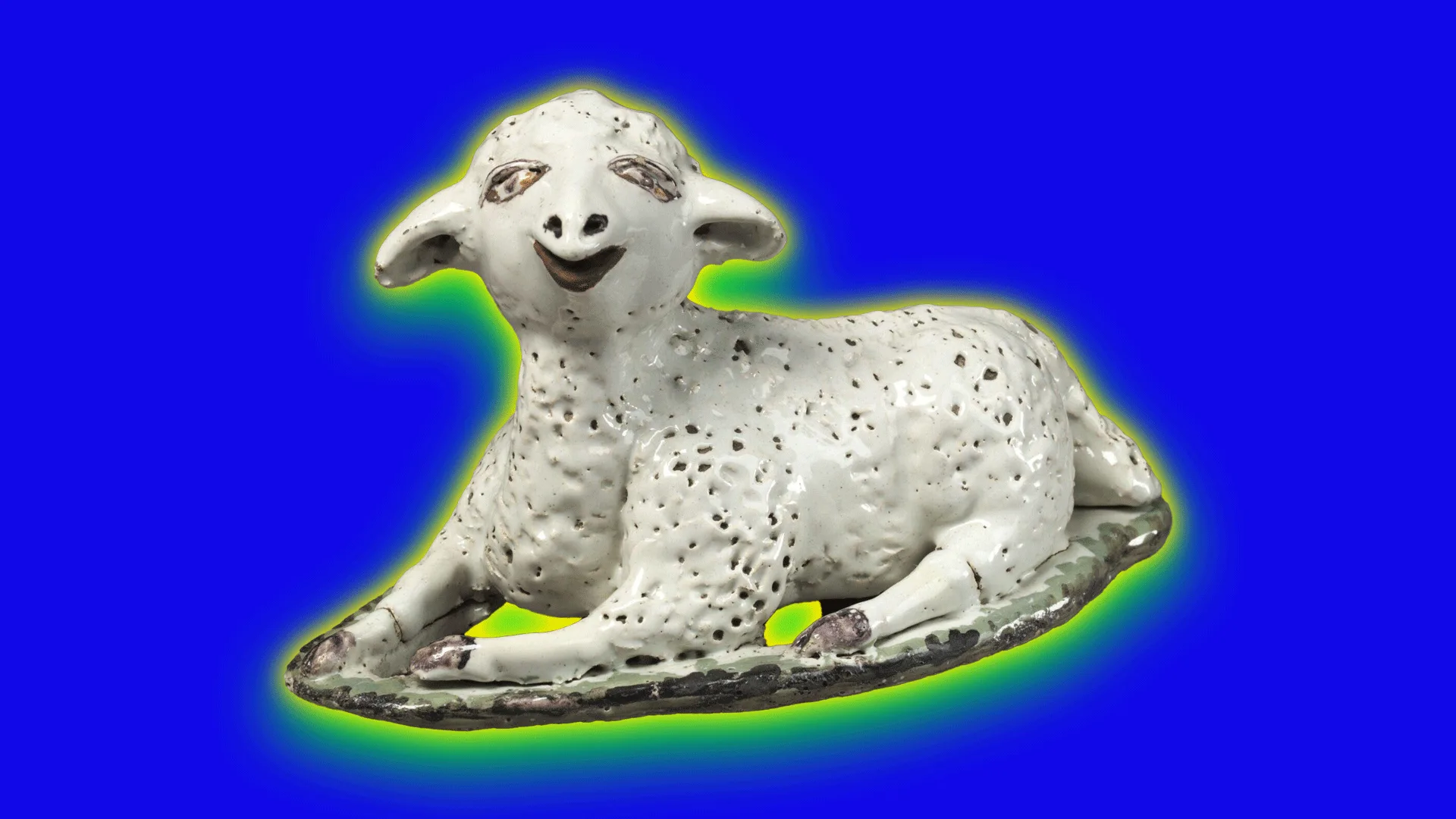 A photo of a ceramic lamb from the 16th century. The lamb is lying on a mount of soil with a smile on it's face against a blue background with a green halo.