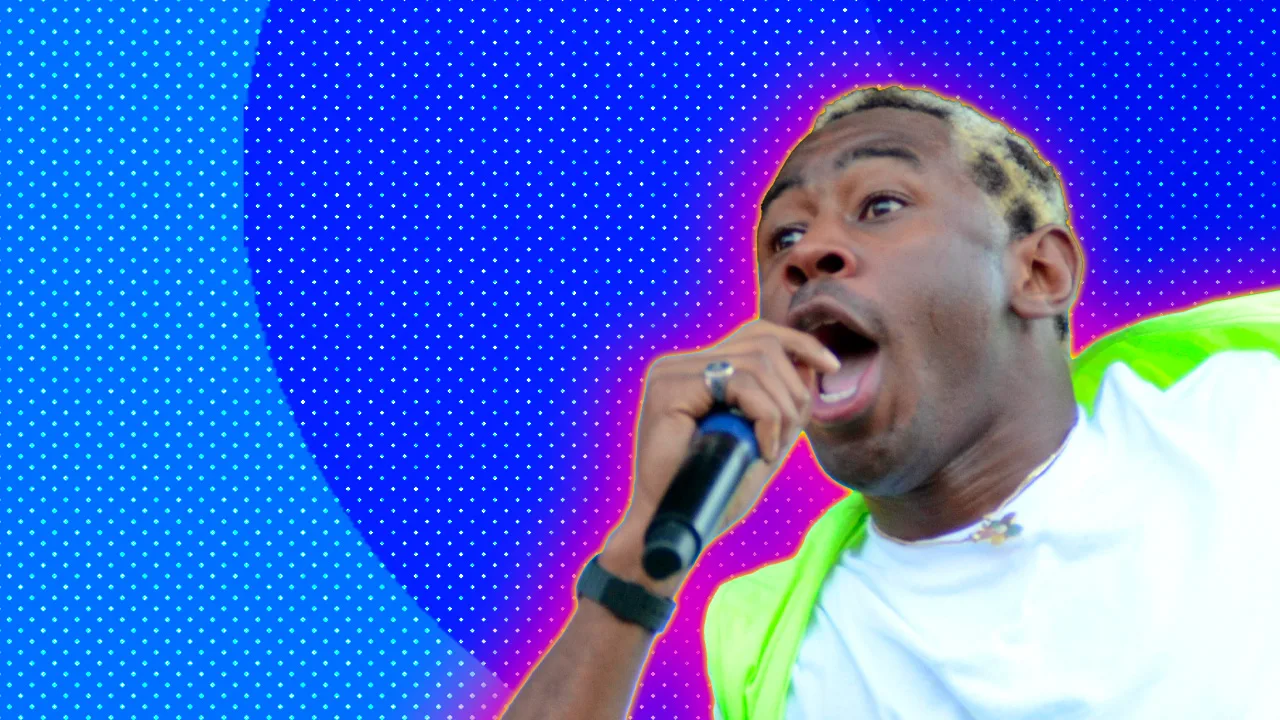 A photo of Tyler the Creator singing into a mic wearing a white tshirt and green jacket set against a blue dotted background with a pink halo.