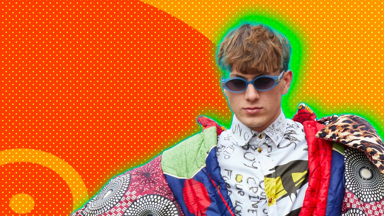 An image of a man wearing sunglasses and a clash of patterns and colours shirt and jacket set against an orange dotted background with a green halo around him.