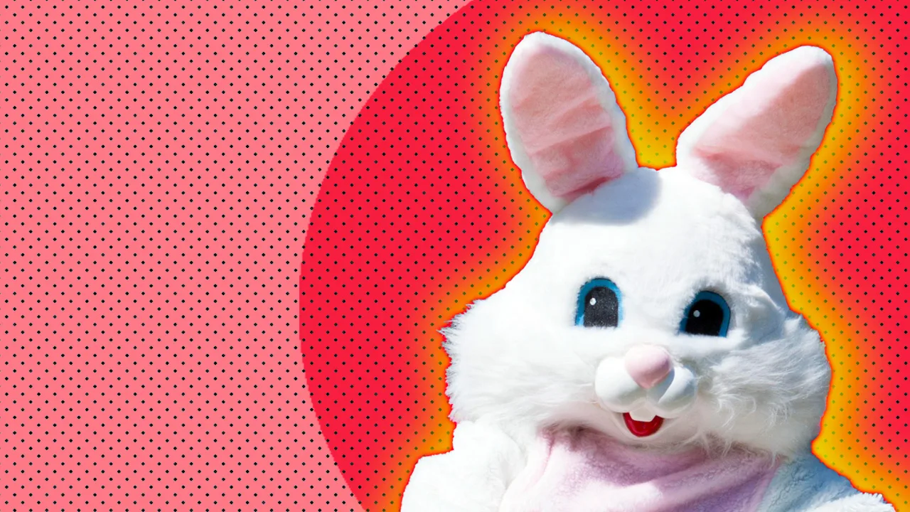 An image of a person dressed as a giant white bunny rabbit with blue eyes and pink ears set against a pink circular dotted background with a yellow orange halo.